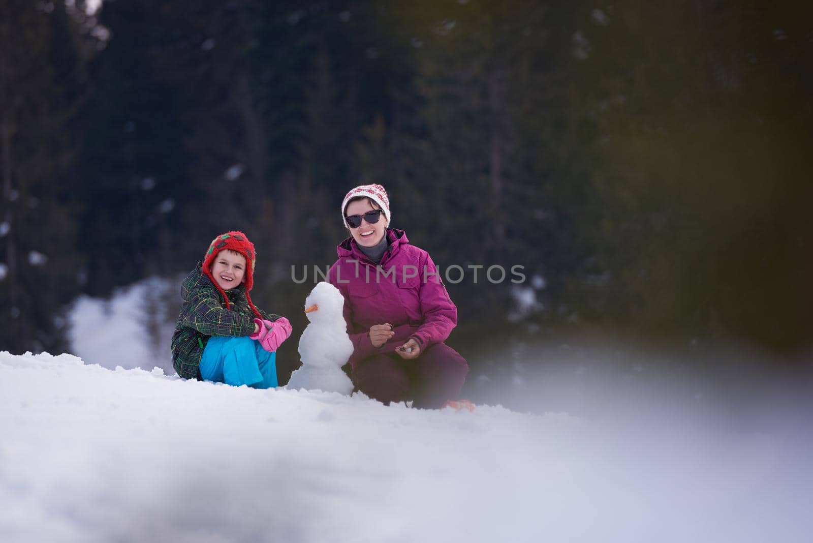 happy young  family playing in fresh snow and building snowman at beautiful sunny winter day outdoor in nature