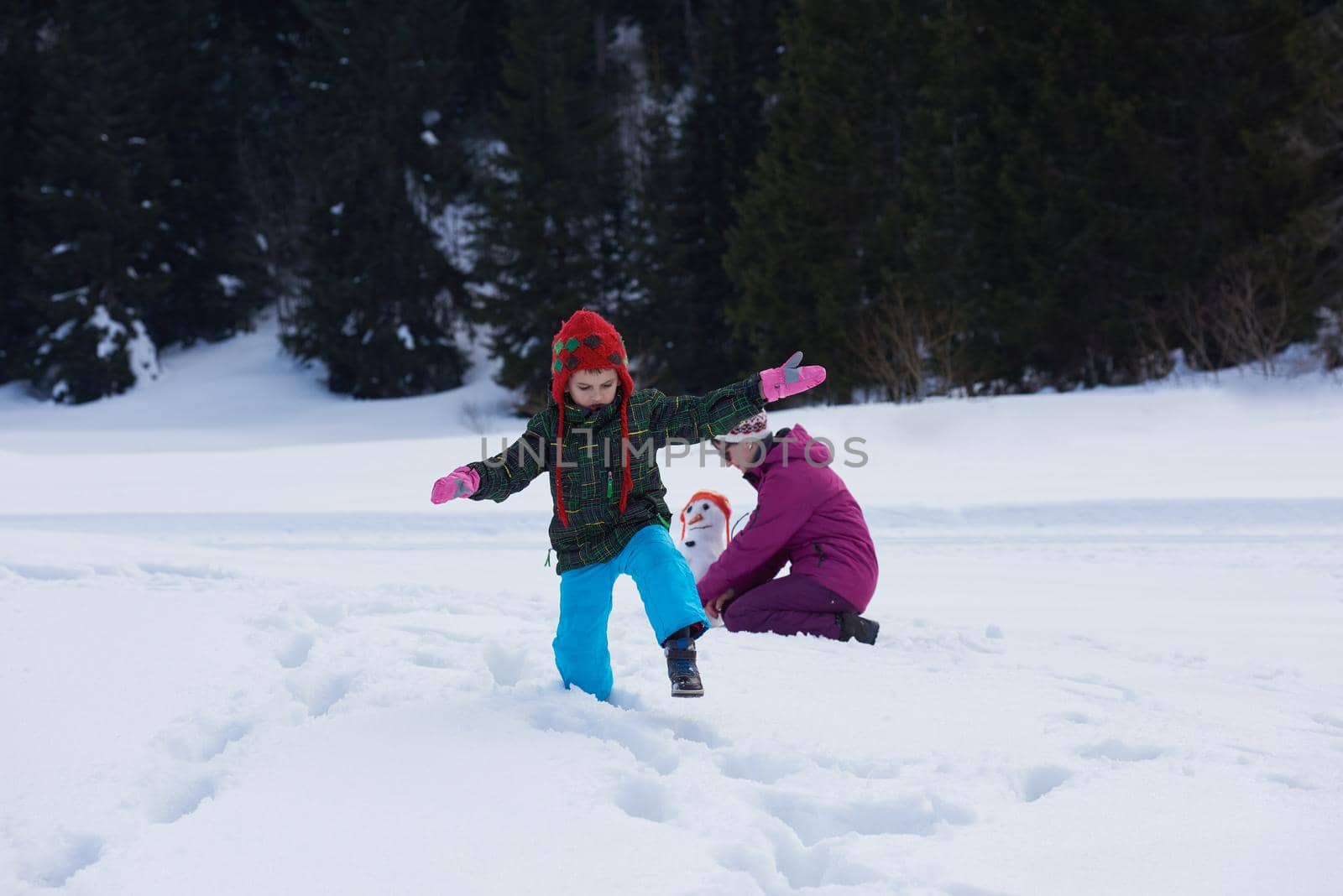 happy young  family playing in fresh snow and building snowman at beautiful sunny winter day outdoor in nature