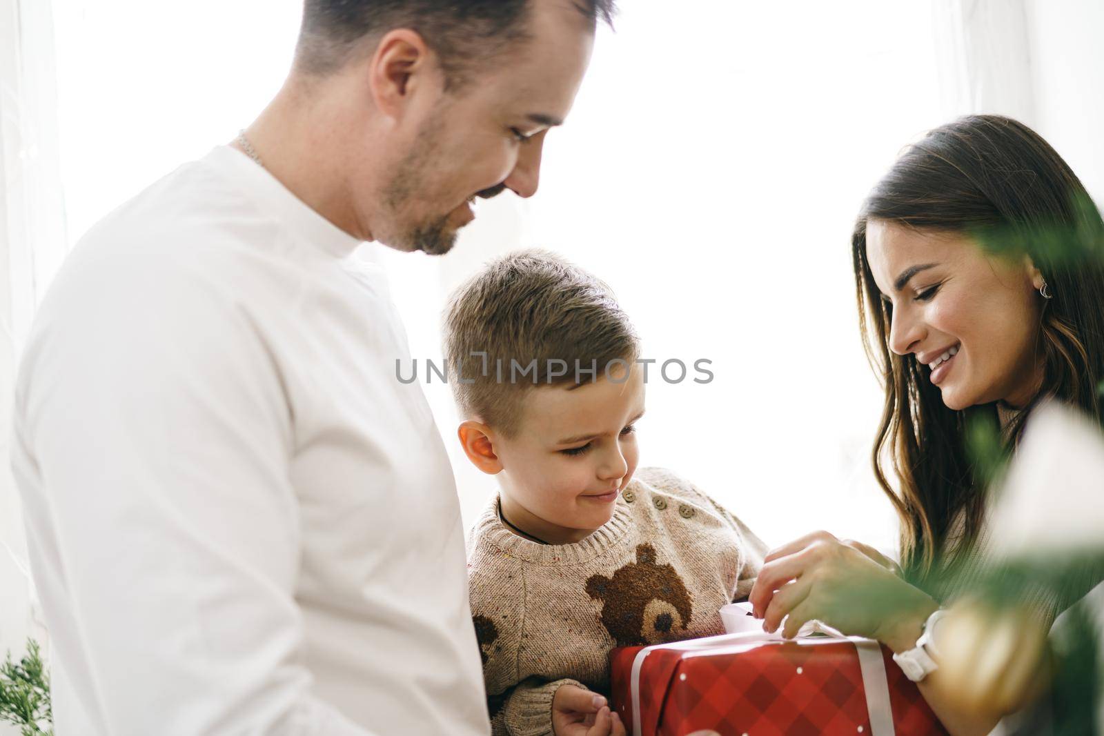 Smiling parents giving Christmas present to son at home, portrait