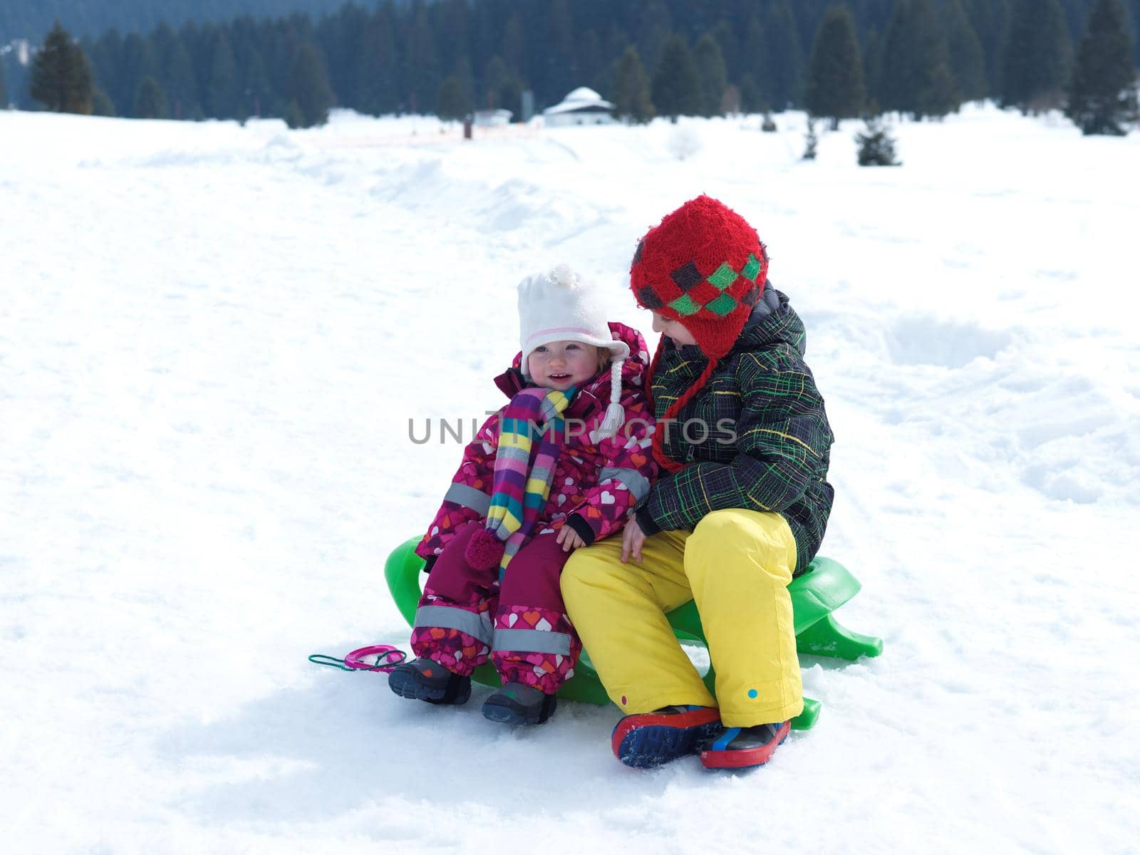 portrait of boy and baby girl on winter vacation sitting on sleddge with fresh snow on beautiful sunny day