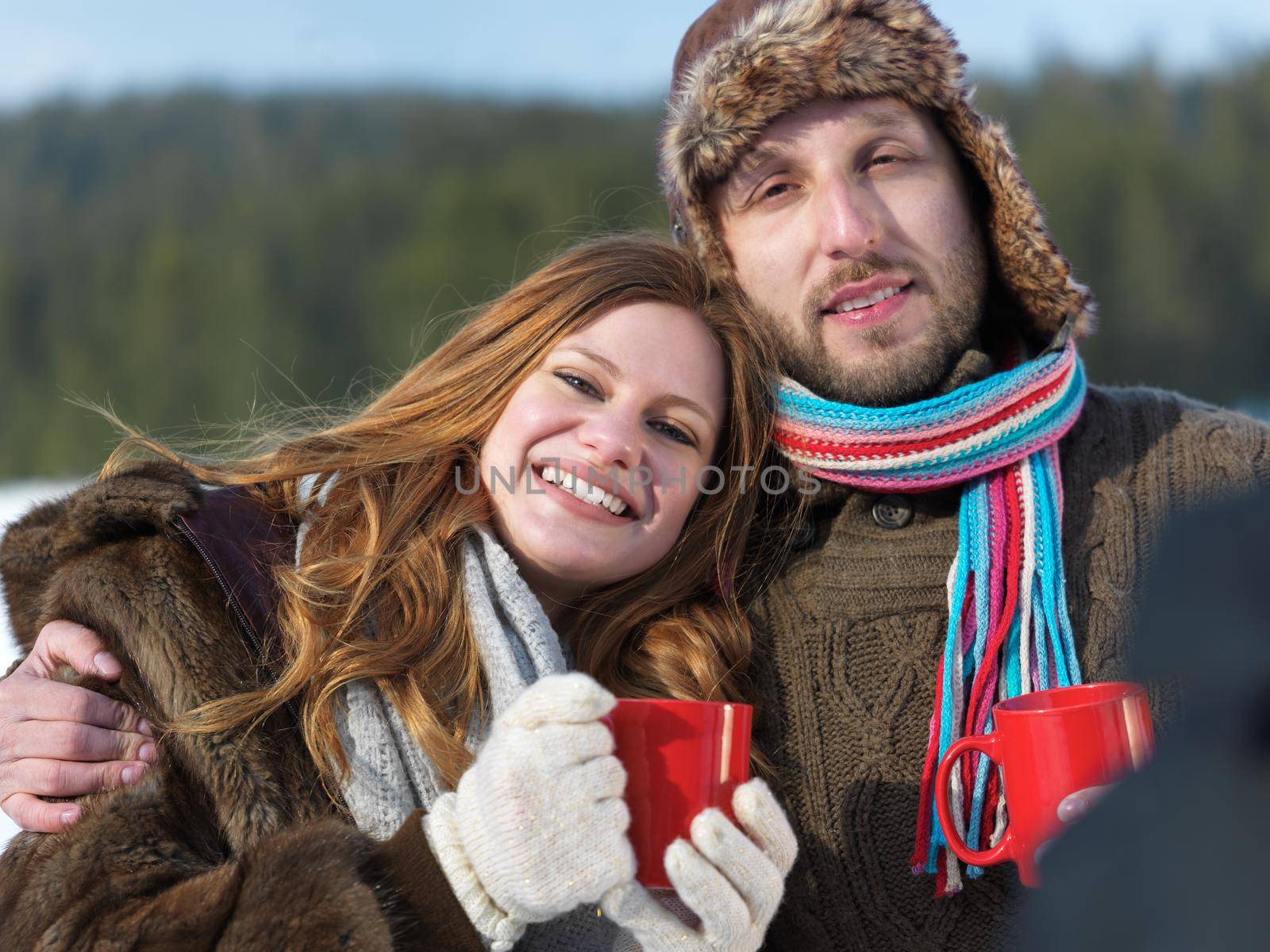 portrait of happy young couple outdoor on winter day drinking warm tea with fresh snow in background