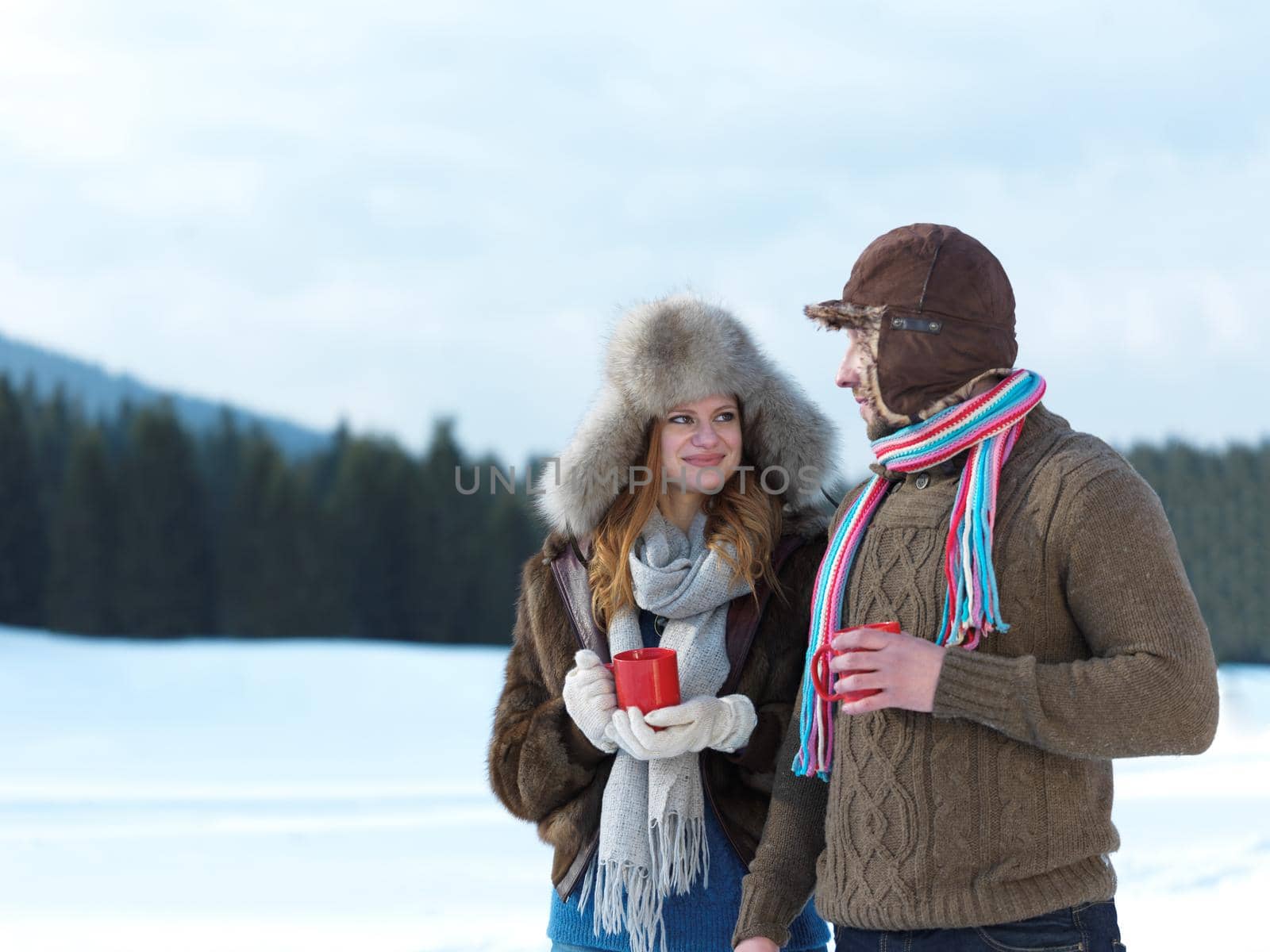 portrait of happy young couple outdoor on winter day drinking warm tea with fresh snow in background