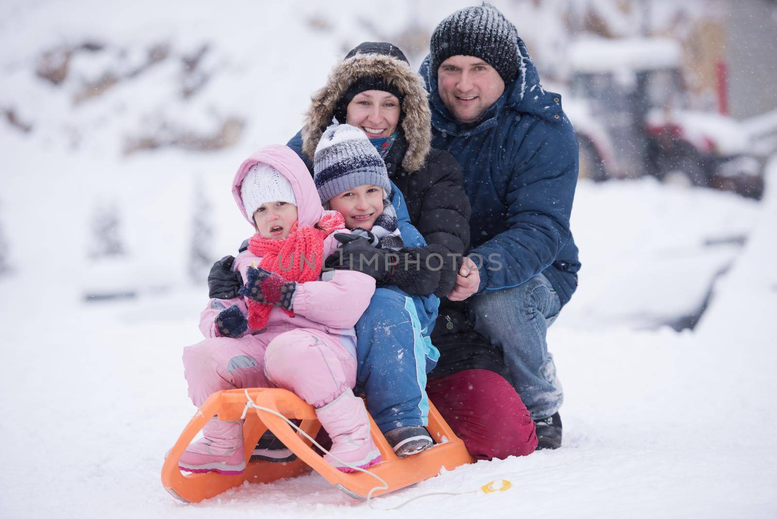 happy young family portrait on winter vacation while sitting sledge at  landscape with fresh falling snow