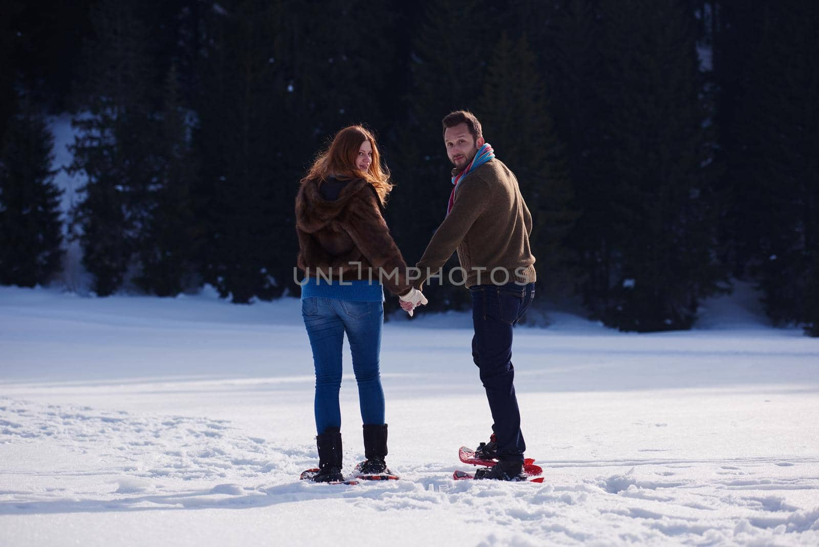 happy young  couple having fun and walking in snow shoes. Romantic winter relaxation scene