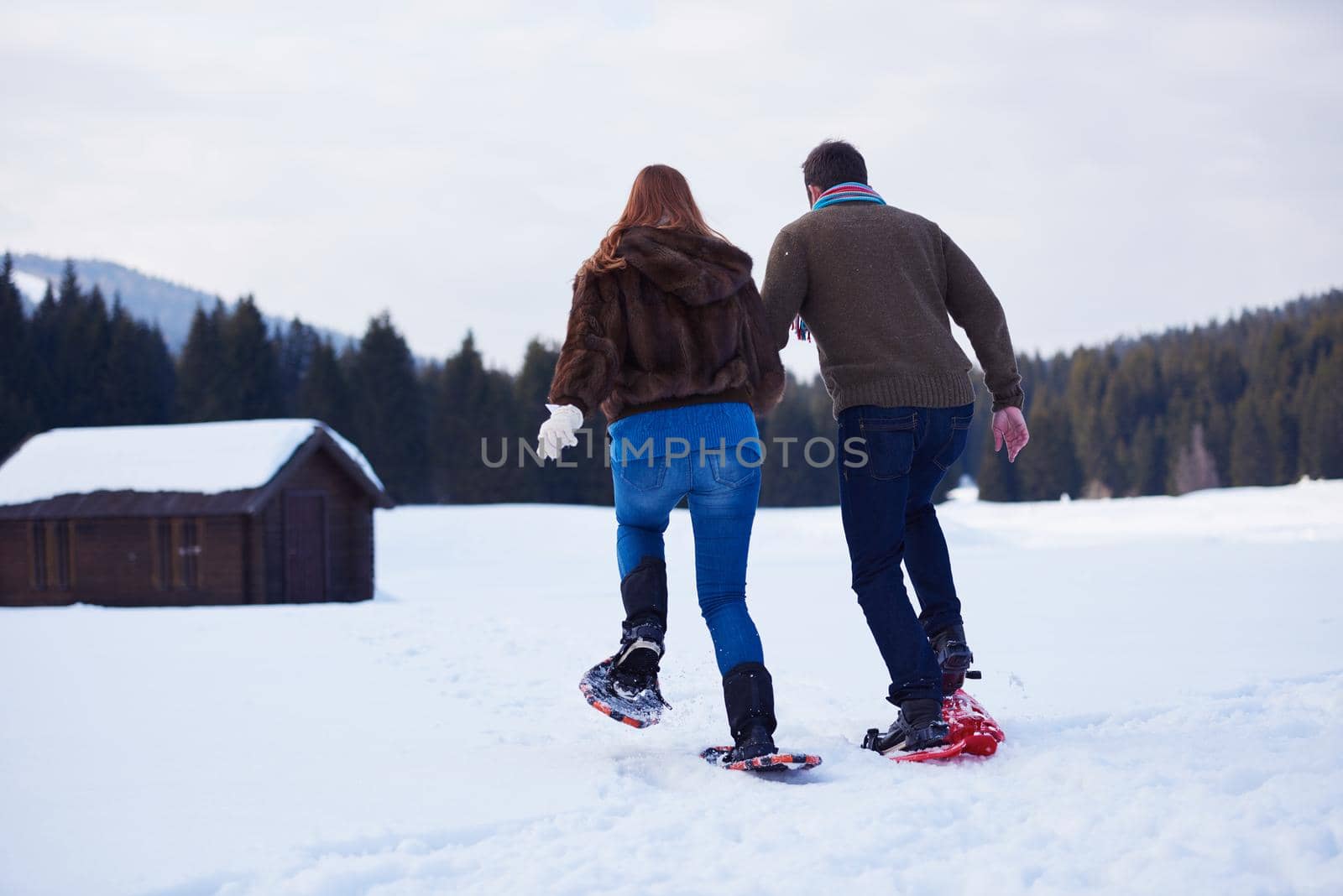 happy young  couple having fun and walking in snow shoes. Romantic winter relaxation scene