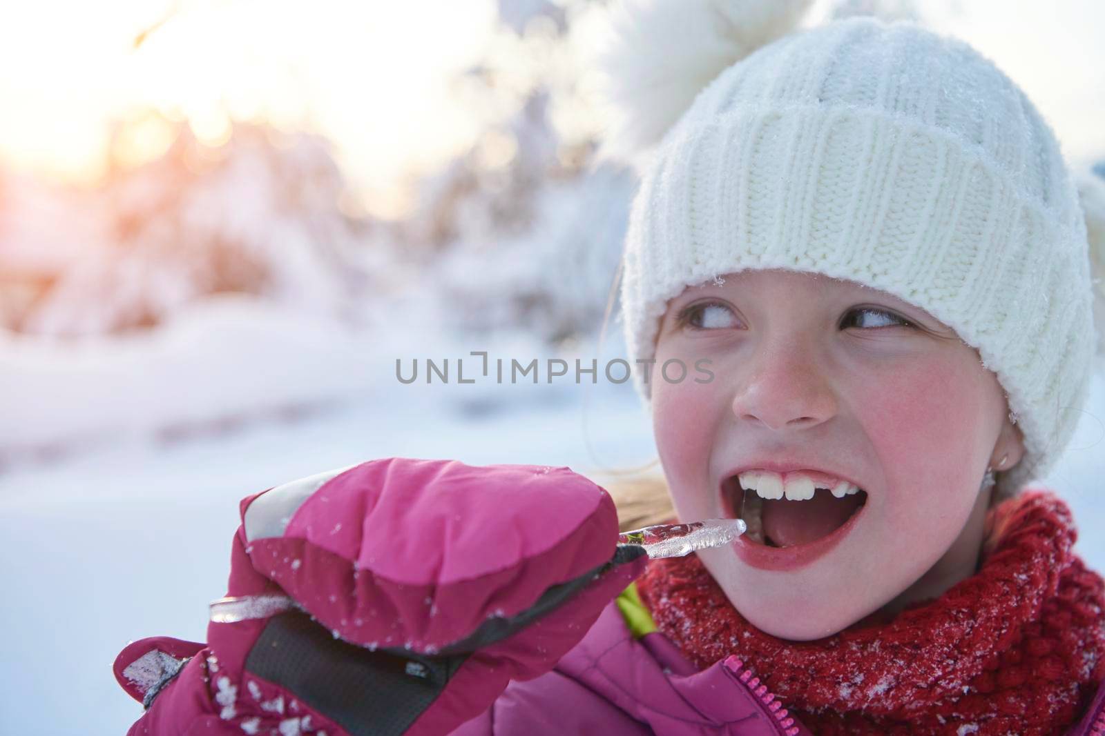 portrait of cute little girl  while eating icicle  on beautiful winter day with fresh snow