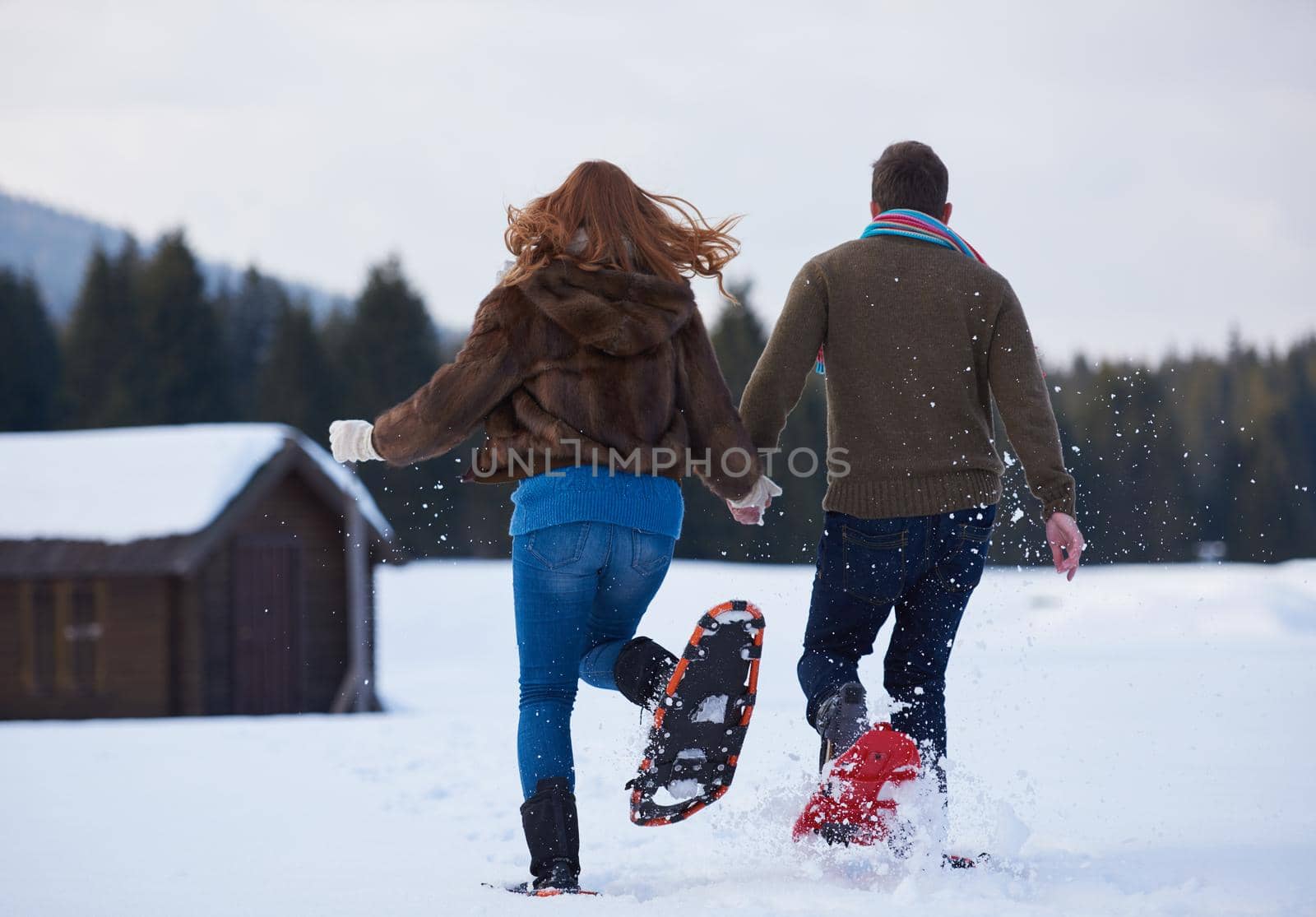 happy young  couple having fun and walking in snow shoes. Romantic winter relaxation scene