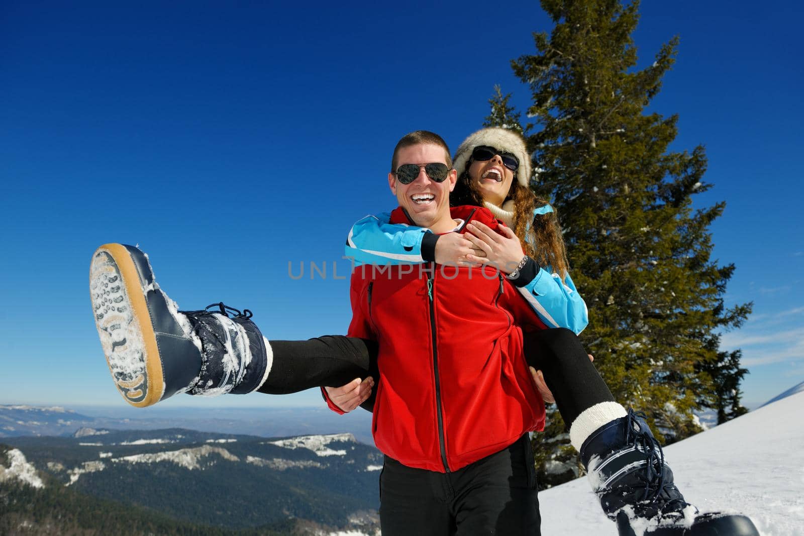 Happy young couple has fun on fresh snow at beautiful winter sunny day on vacation