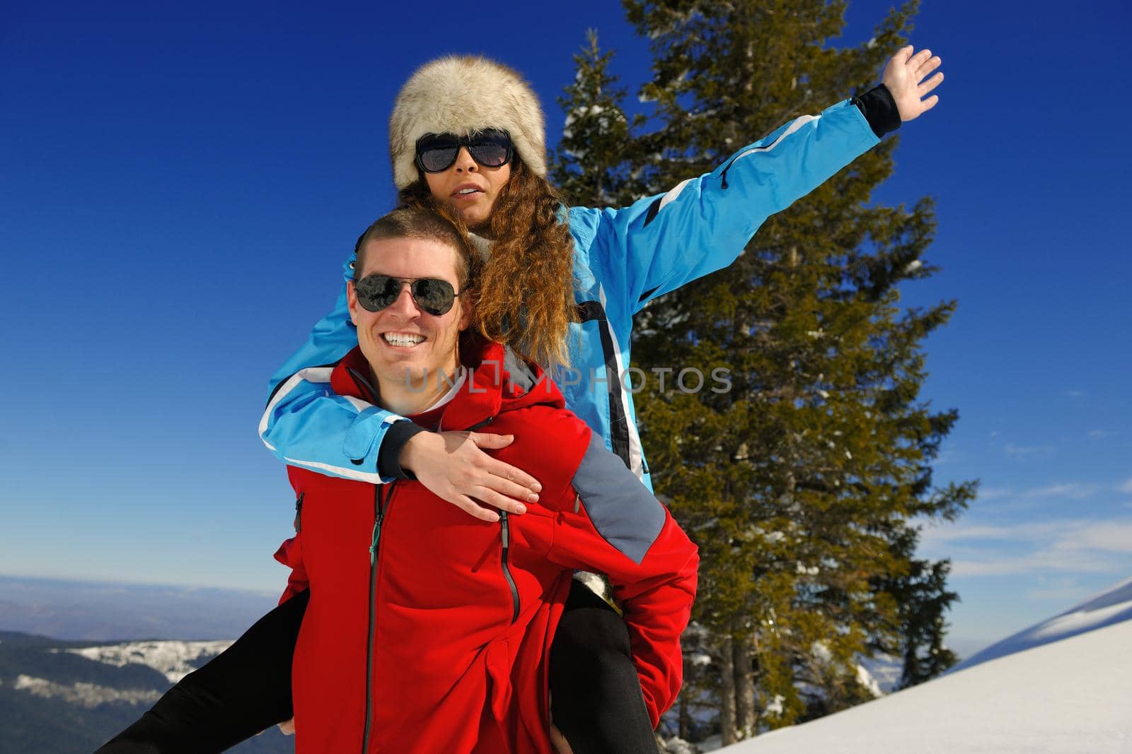 Happy young couple has fun on fresh snow at beautiful winter sunny day on vacation