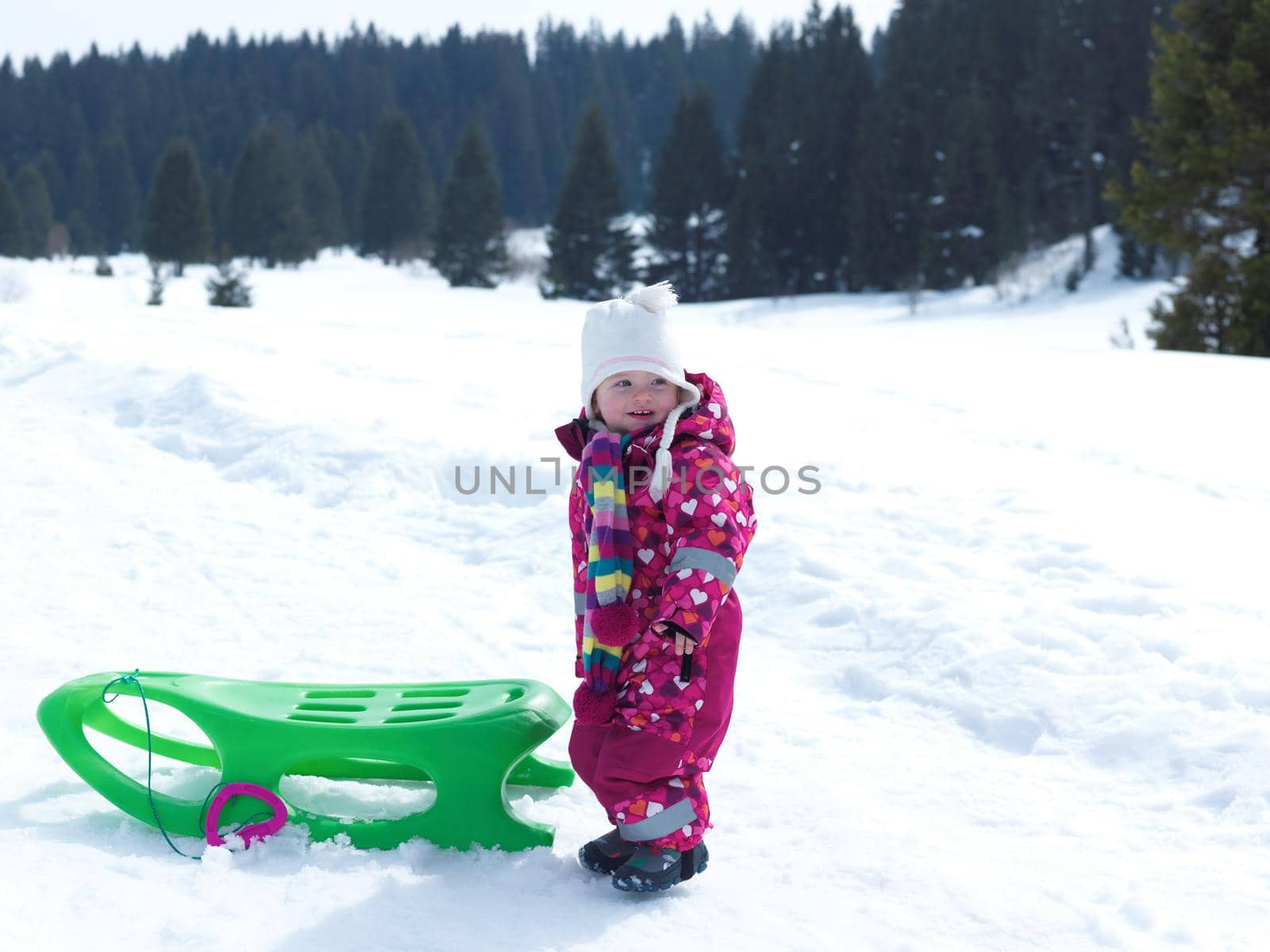 little baby girl have fun on fresh snow and slide on sleddges at beautiful sunny winter day