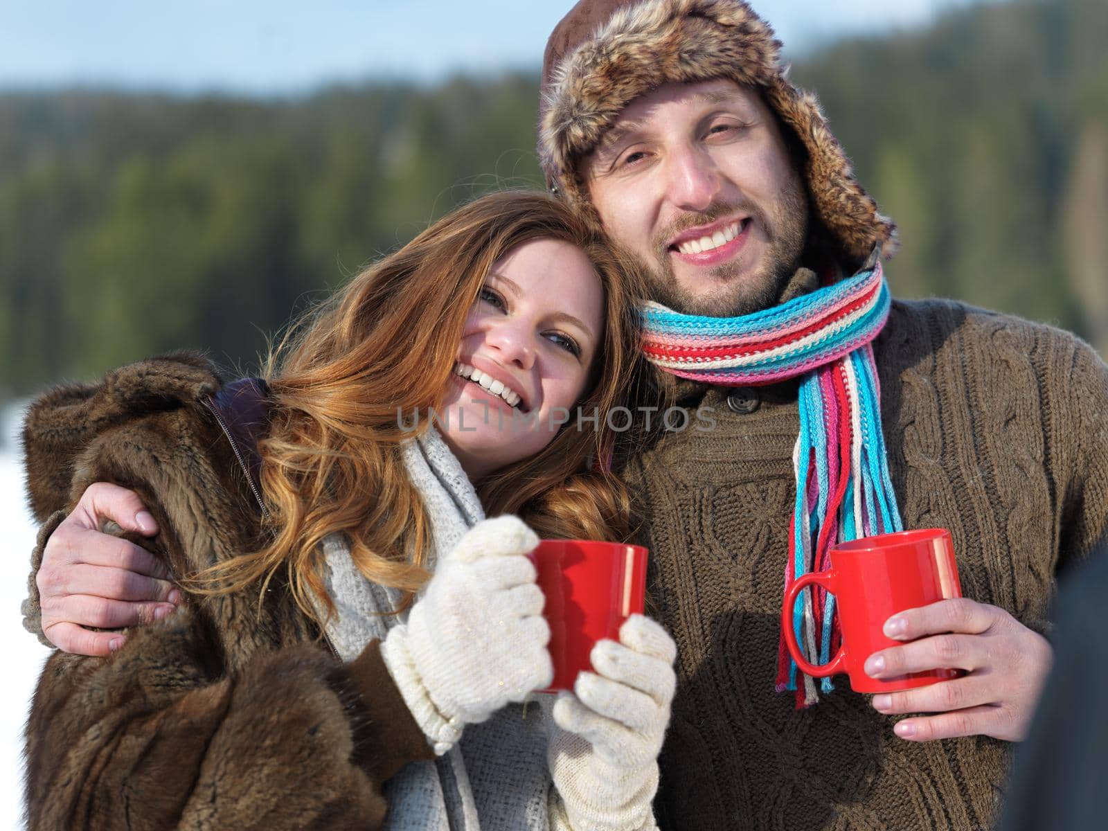 portrait of happy young couple outdoor on winter day drinking warm tea with fresh snow in background