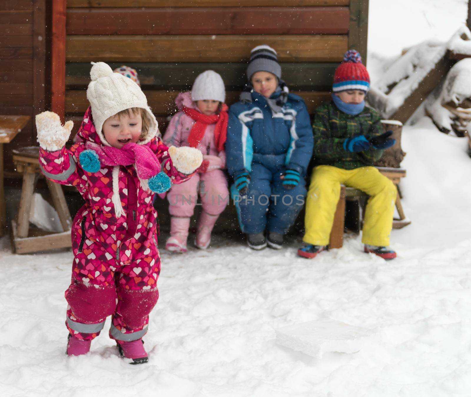 group portrait of kids, little child  group sitting together  in front of wooden cabin on vacation at beautiful winter  day with fresh snow