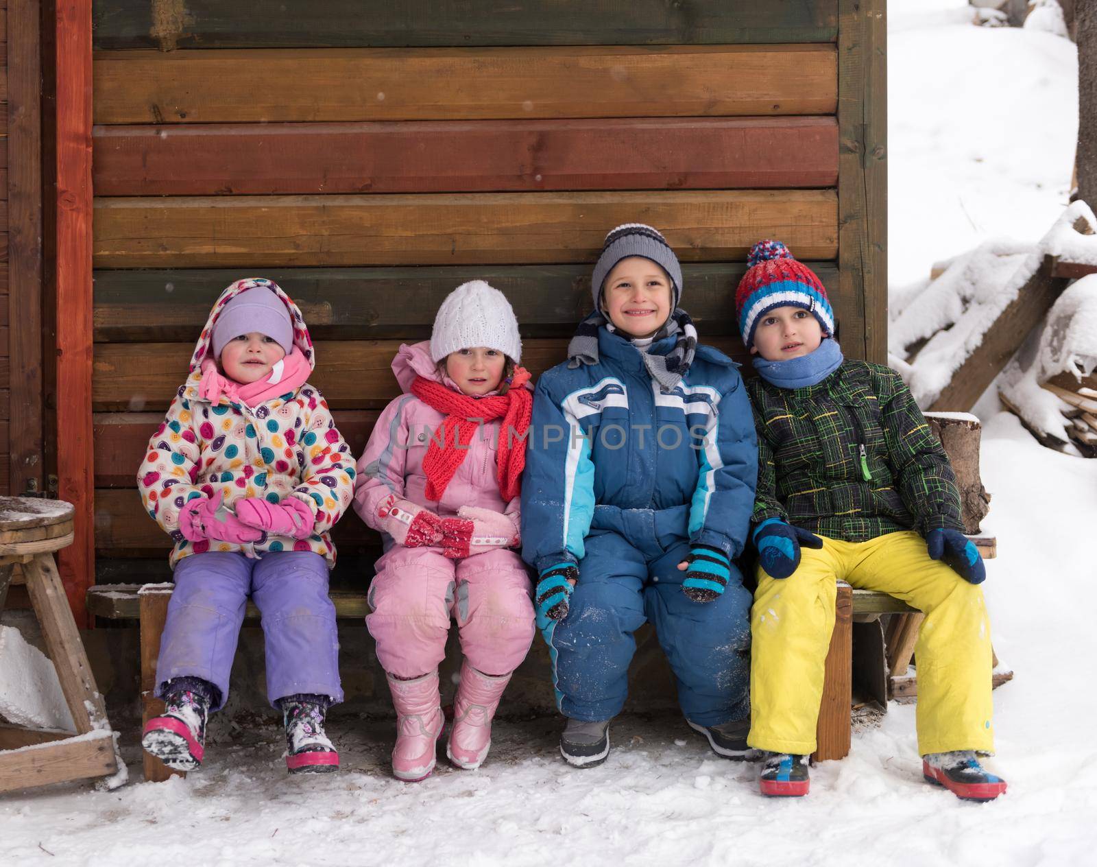 group portrait of kids, little child  group sitting together  in front of wooden cabin on vacation at beautiful winter  day with fresh snow