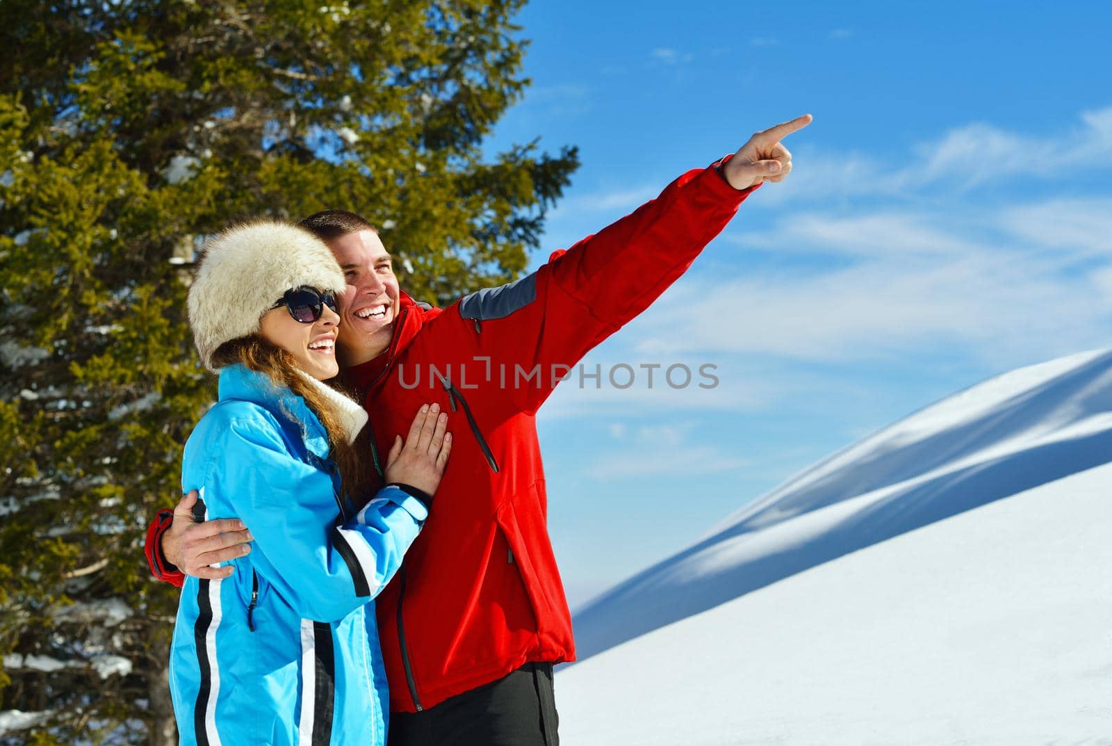 Happy young couple has fun on fresh snow at beautiful winter sunny day on relaxing vacation