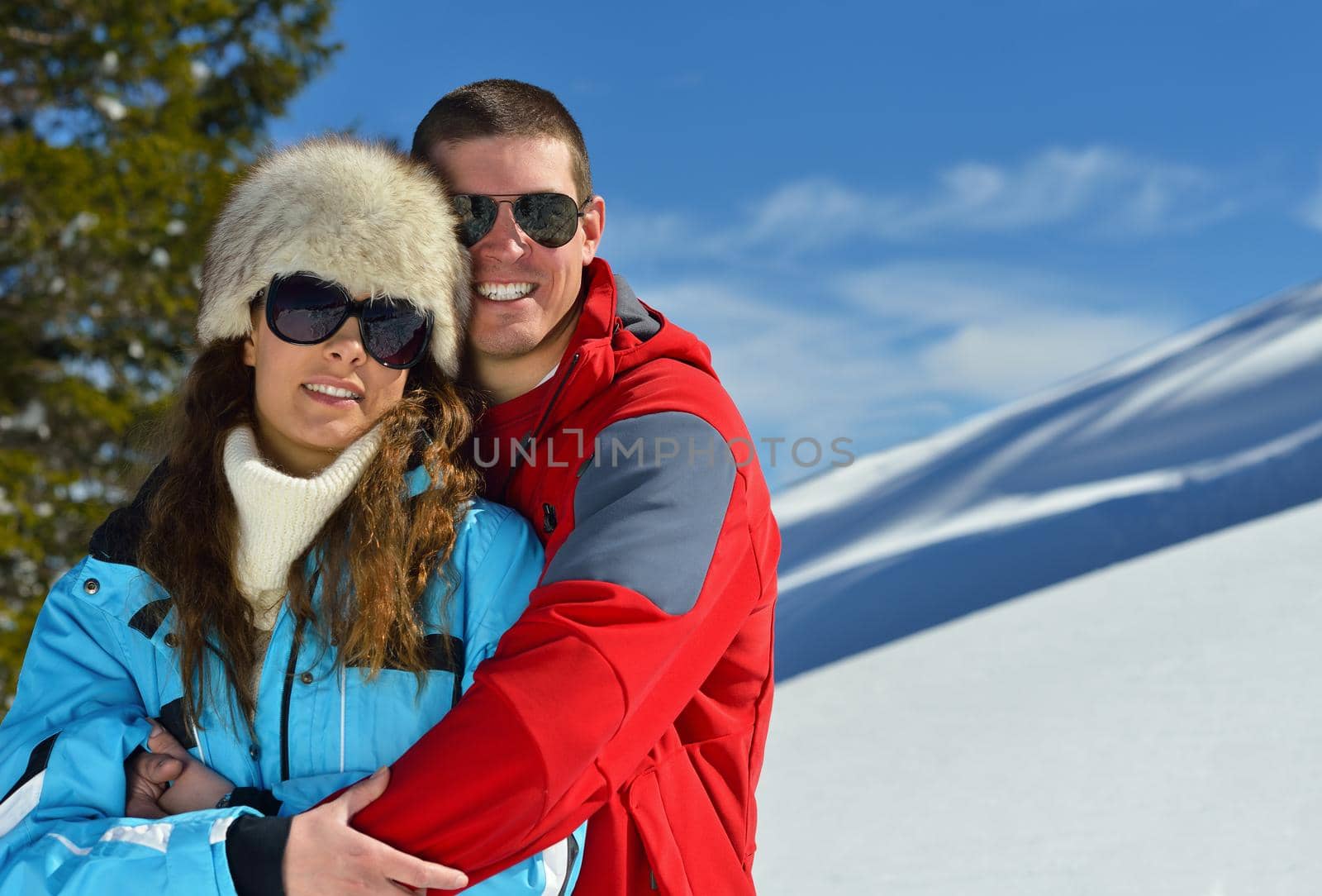 Happy young couple has fun on fresh snow at beautiful winter sunny day on relaxing vacation