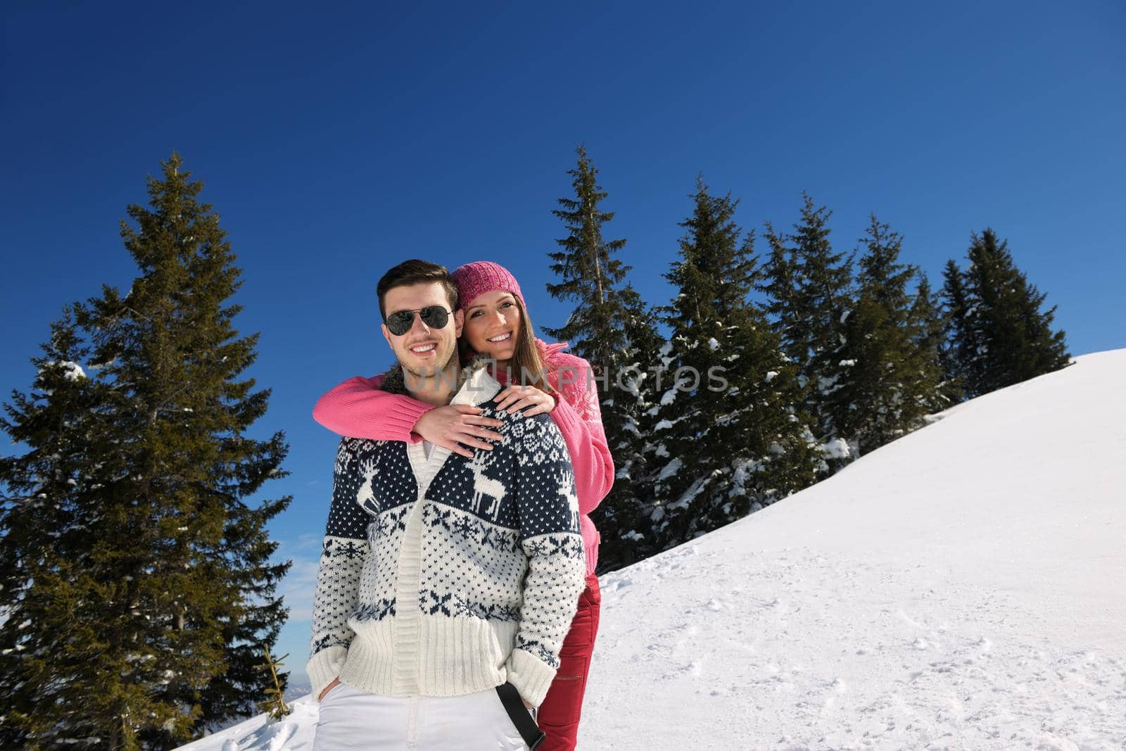 Happy young couple has fun on fresh snow at beautiful winter sunny day on vacation