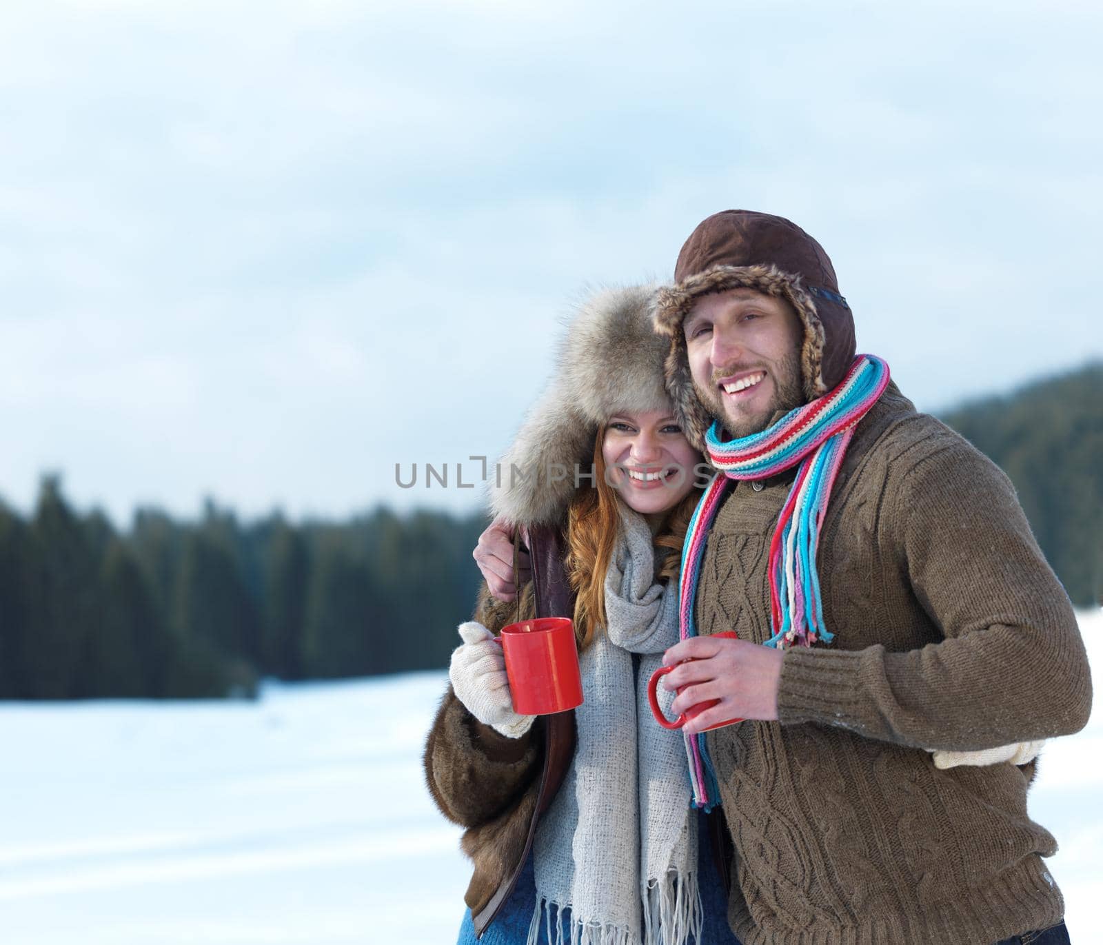 portrait of happy young couple outdoor on winter day drinking warm tea with fresh snow in background