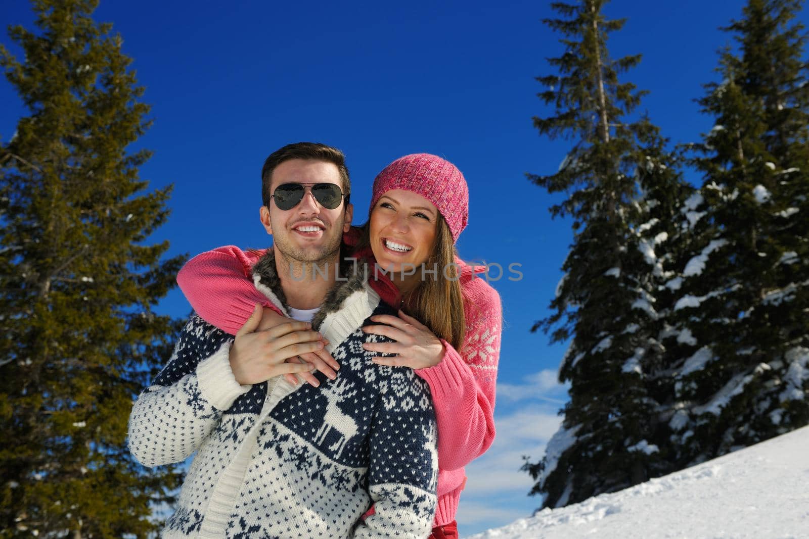 Happy young couple has fun on fresh snow at beautiful winter sunny day on vacation