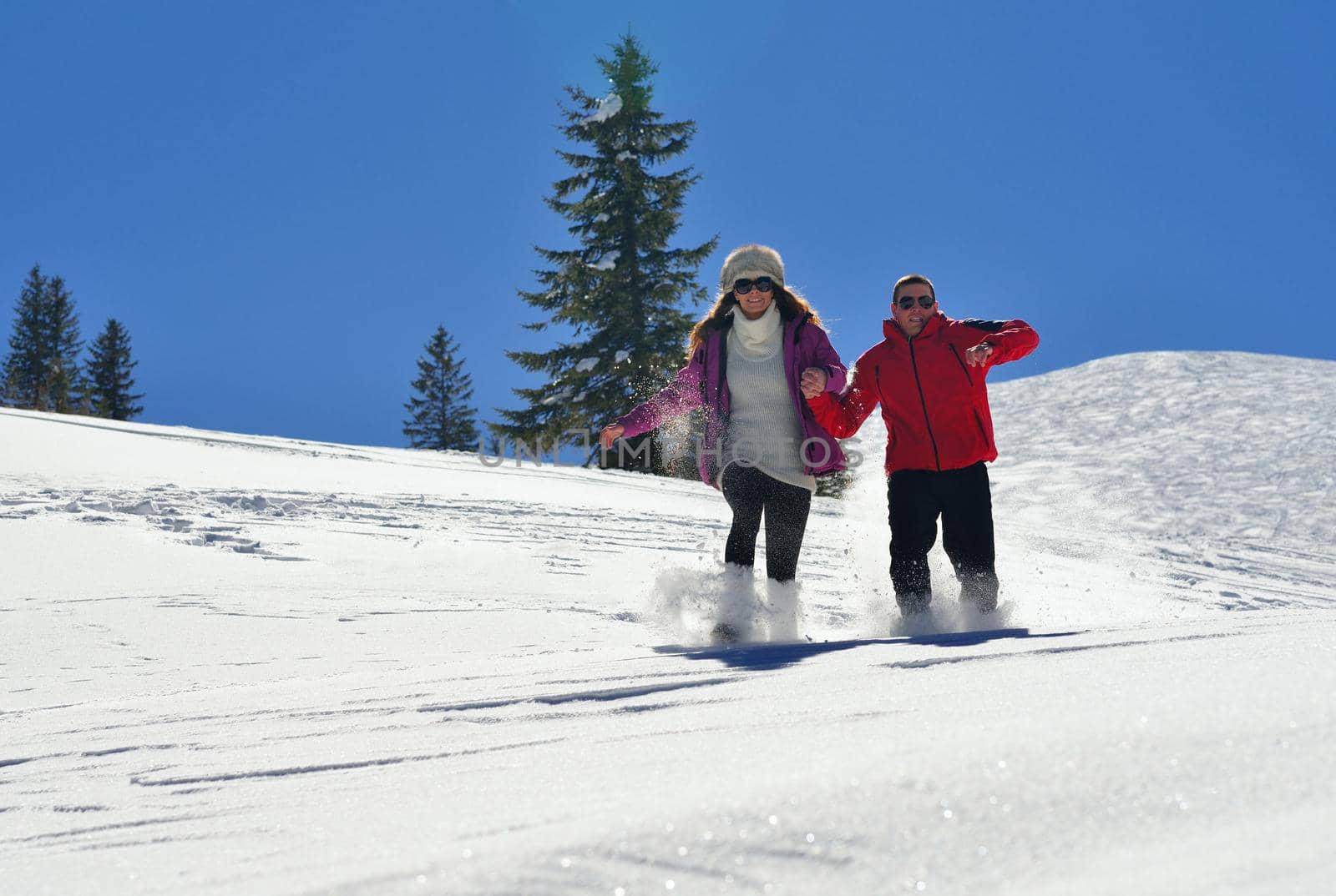 Happy young couple has fun on fresh snow at beautiful winter sunny day on relaxing vacation