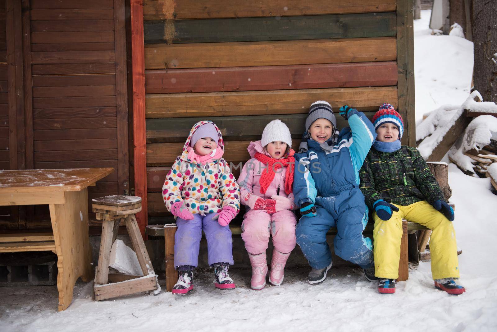 little children group sitting  together  in front of wooden cabin by dotshock