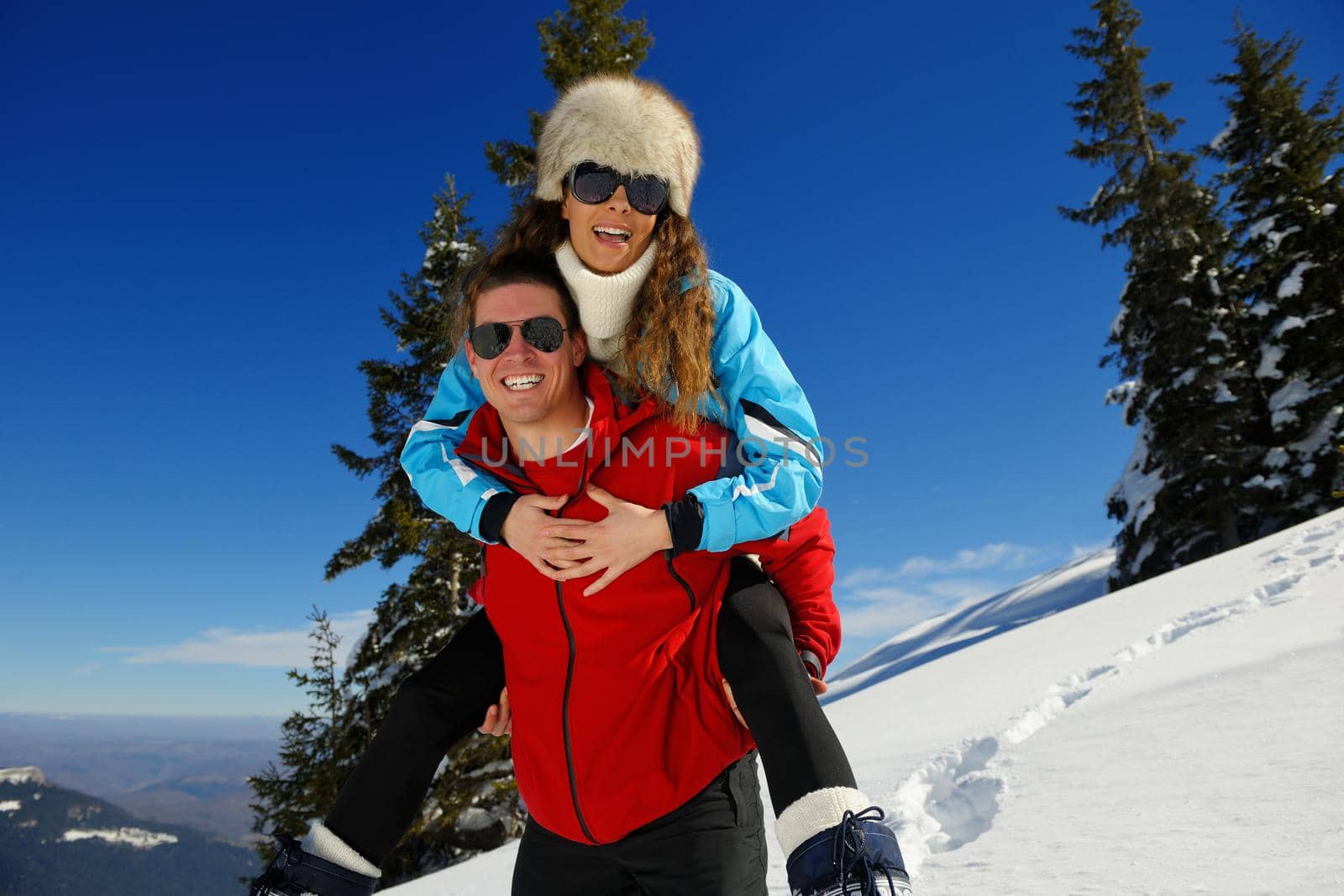 Happy young couple has fun on fresh snow at beautiful winter sunny day on vacation