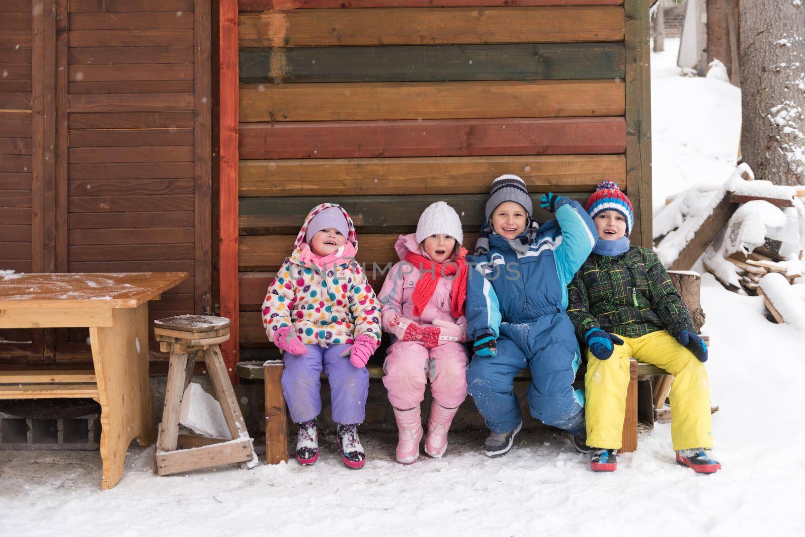 group portrait of kids, little child  group sitting together  in front of wooden cabin on vacation at beautiful winter  day with fresh snow