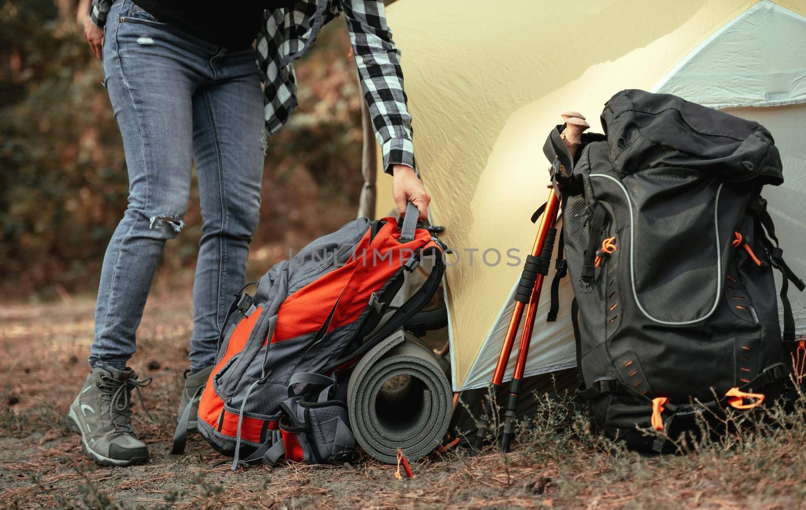 Person preparing to hiking and put on the ground backppacks and karemat close to tent in camping place in the forest. View on travel touristic hiking equipment outdoor