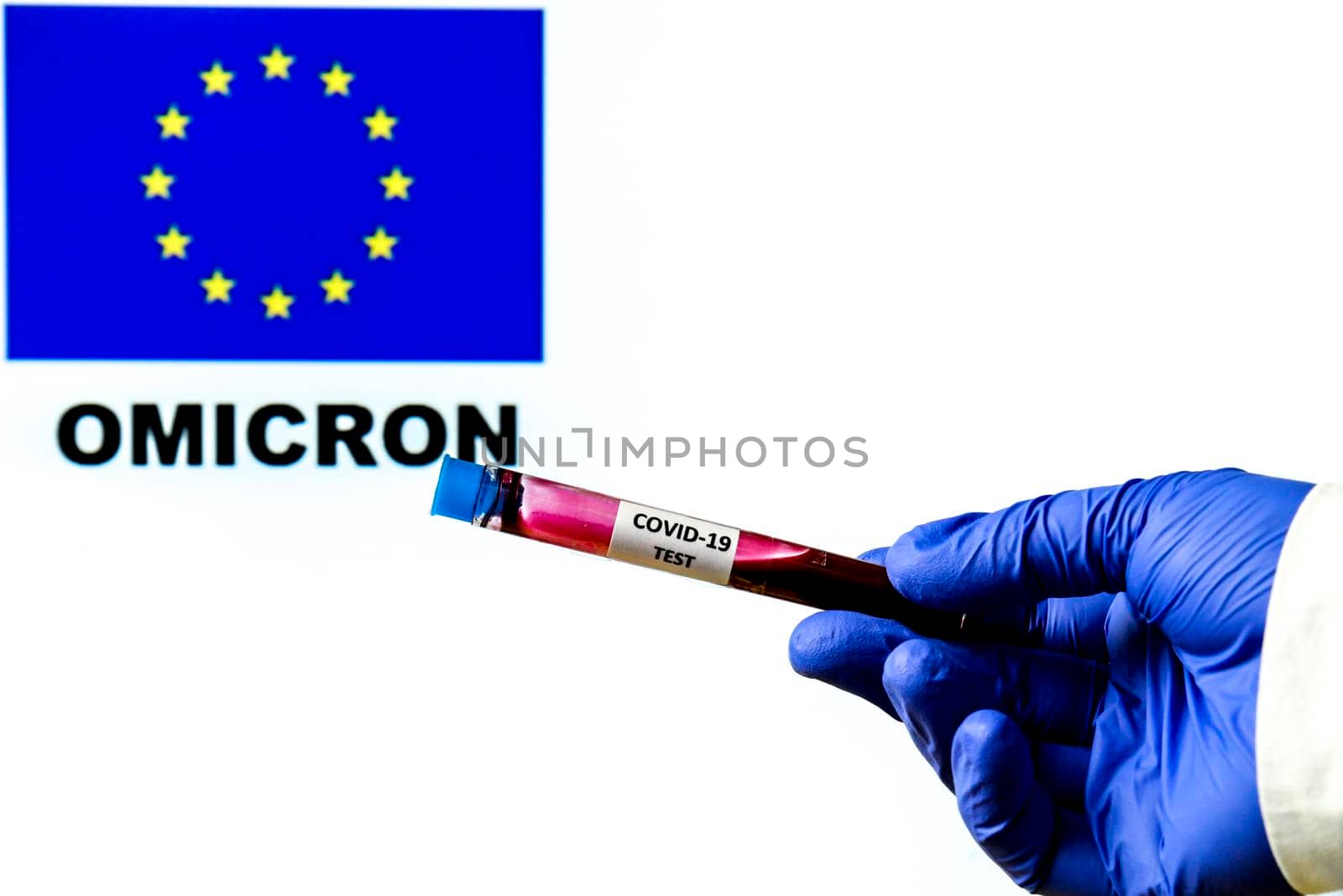 Hand holding test tube of covid-19 virus on white background with European flag and Omicron word written on it
