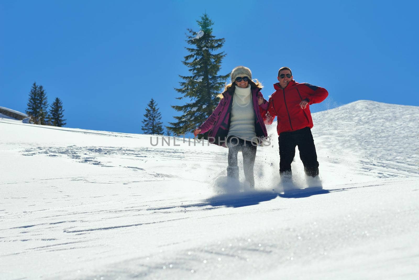 Happy young couple has fun on fresh snow at beautiful winter sunny day on relaxing vacation