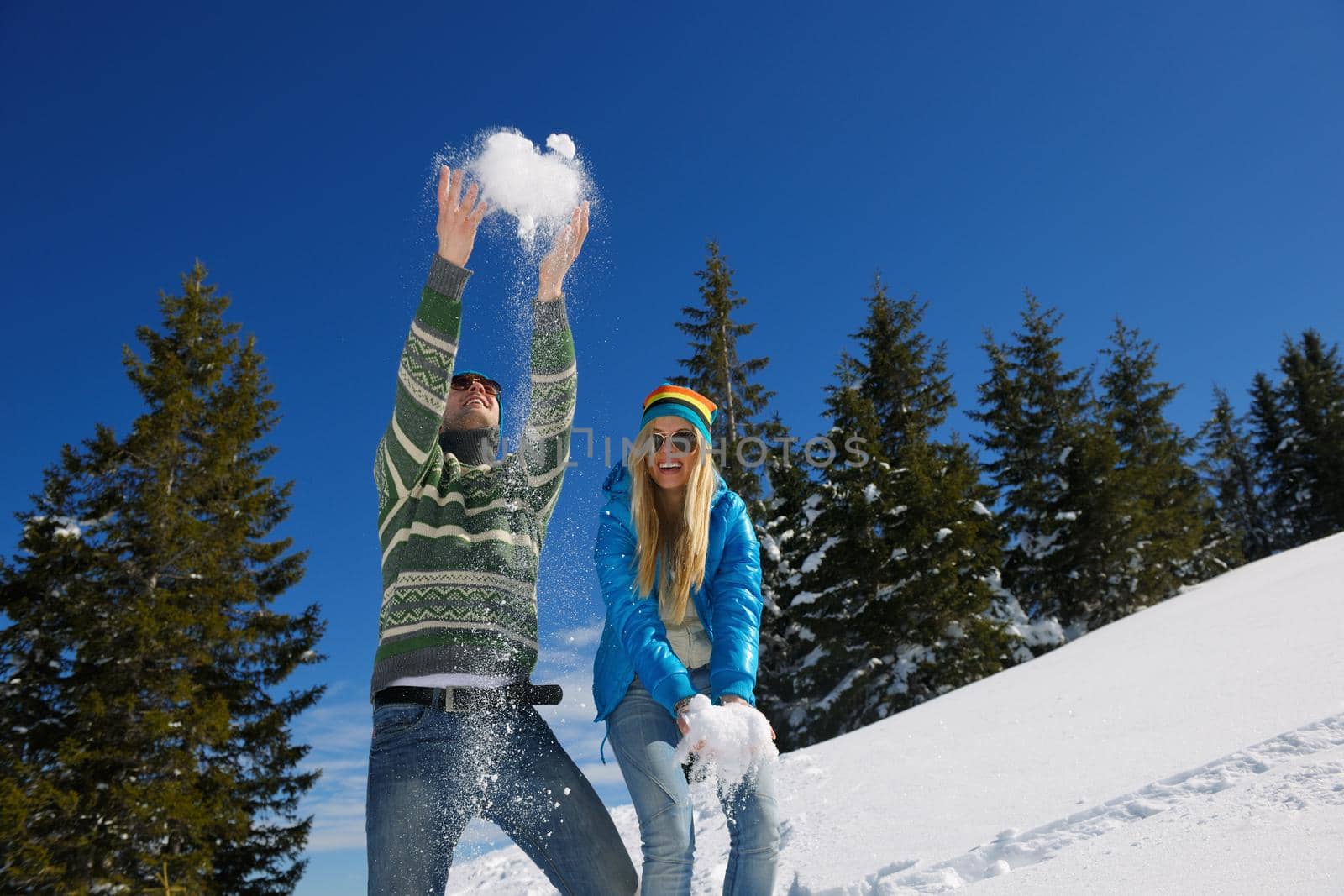 Happy young couple has fun on fresh snow at beautiful winter sunny day on relaxing vacation