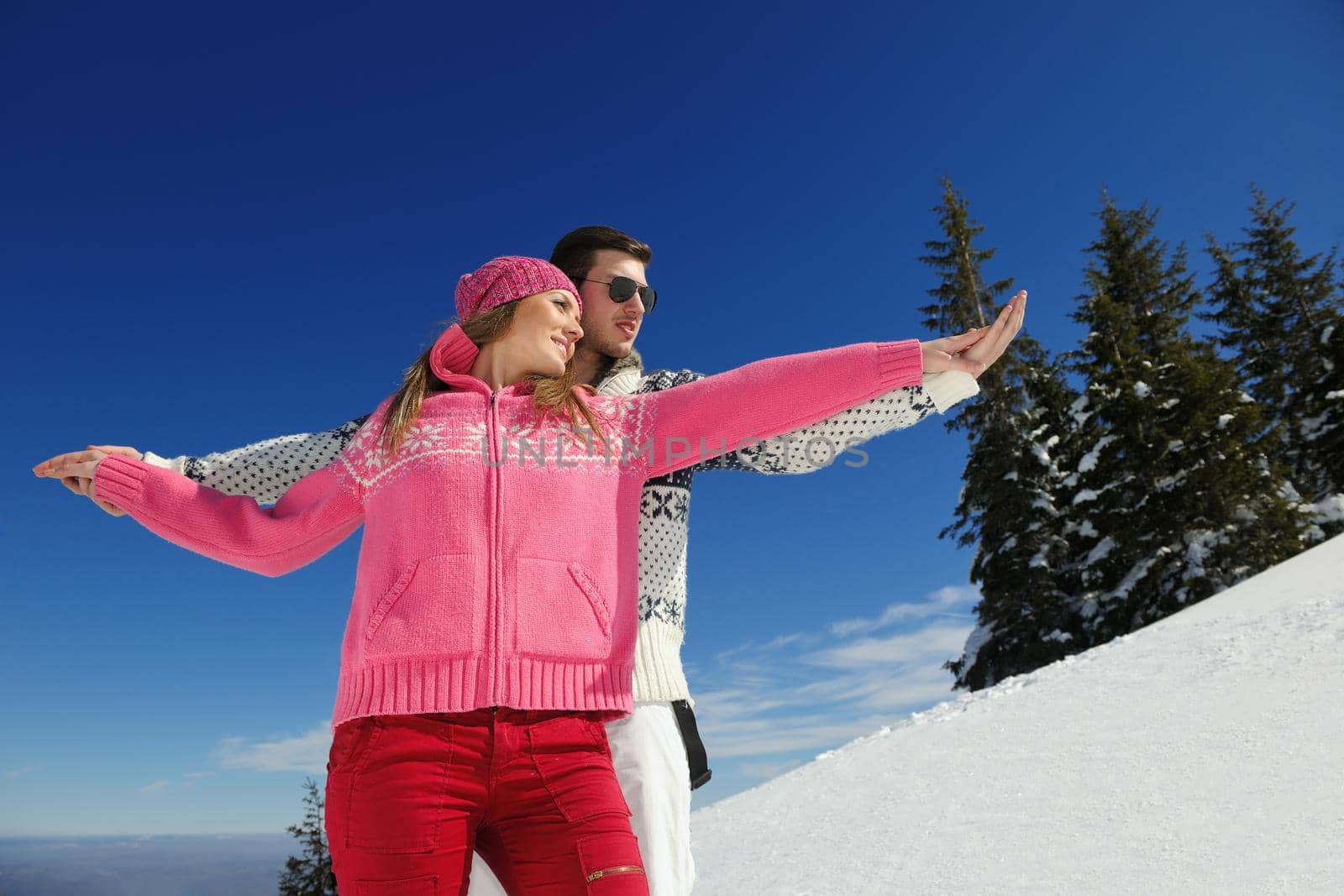 Happy young couple has fun on fresh snow at beautiful winter sunny day on vacation