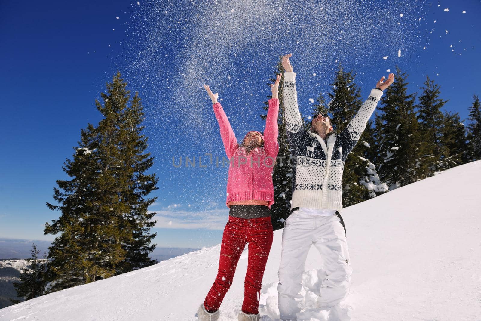 Happy young couple has fun on fresh snow at beautiful winter sunny day on vacation