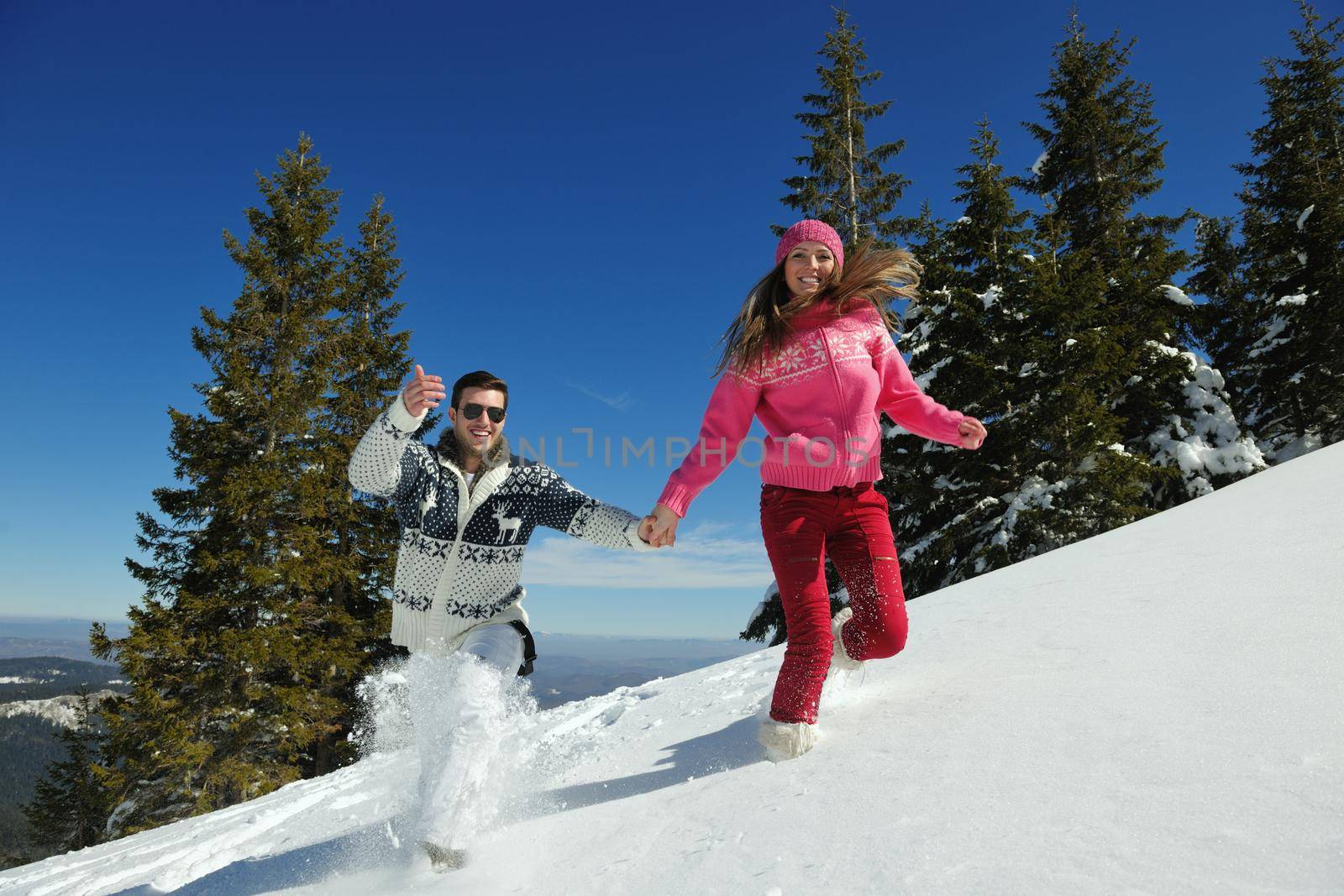 Happy young couple has fun on fresh snow at beautiful winter sunny day on vacation