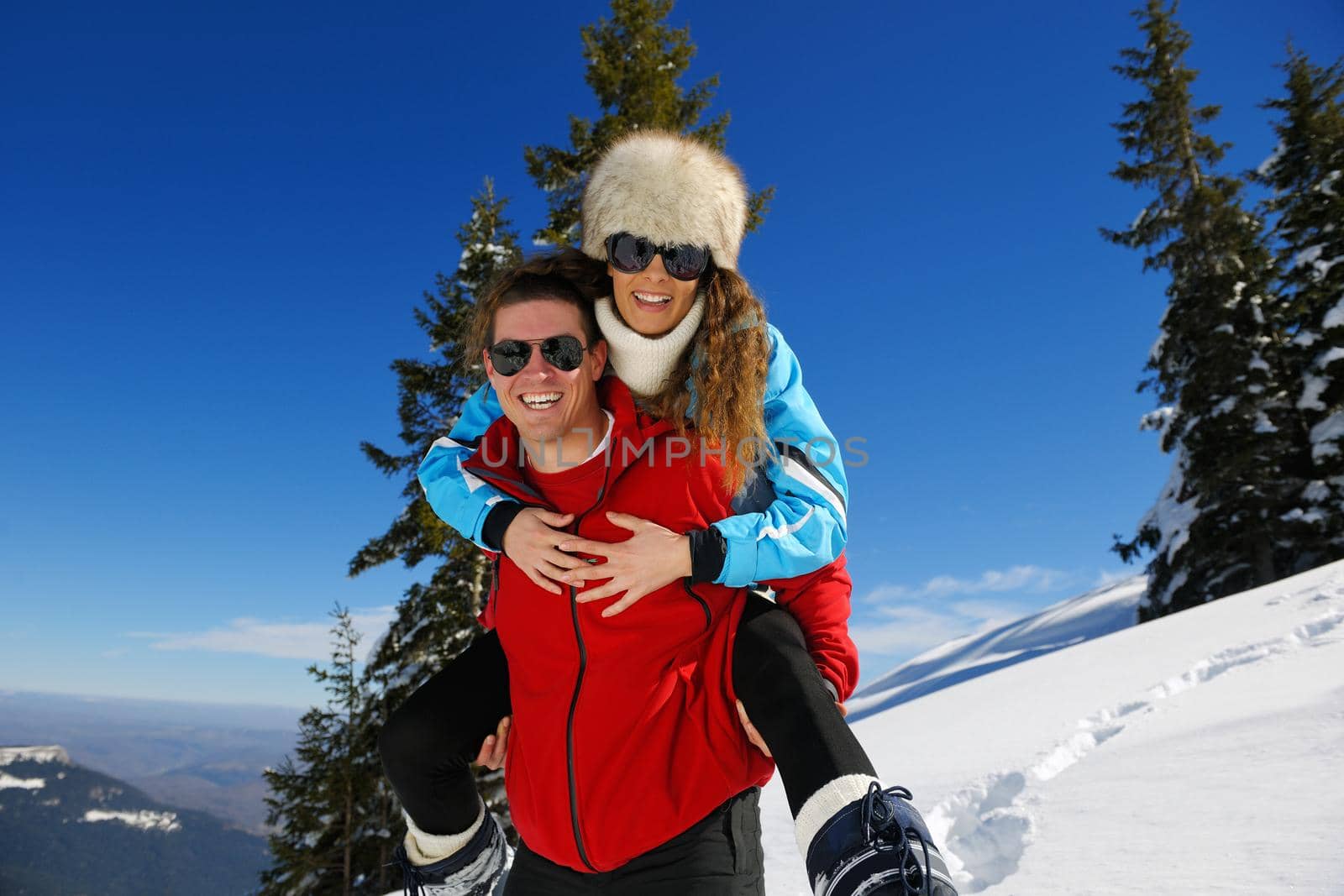 Happy young couple has fun on fresh snow at beautiful winter sunny day on vacation