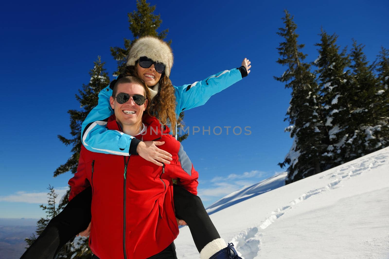 Happy young couple has fun on fresh snow at beautiful winter sunny day on vacation