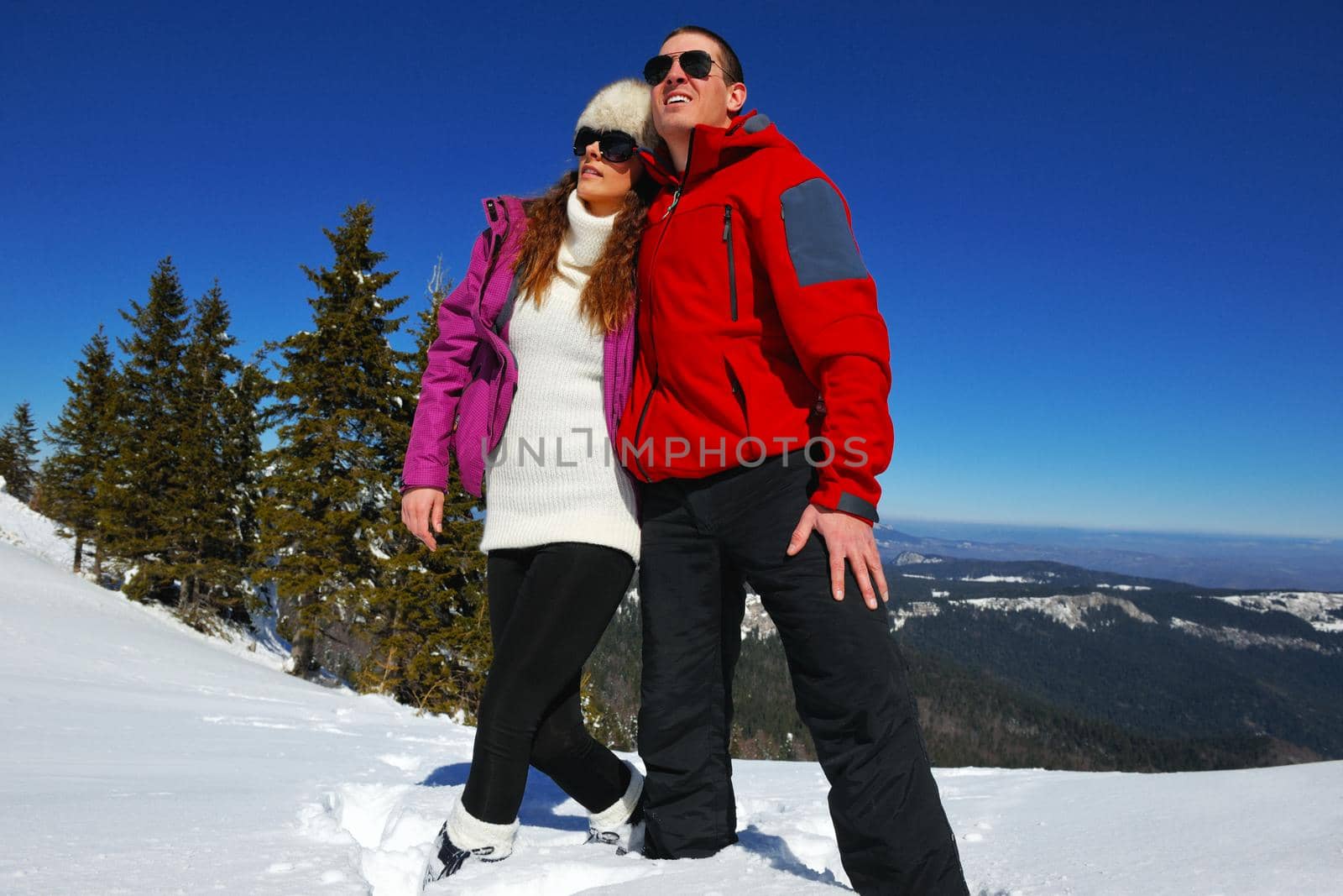 Happy young couple has fun on fresh snow at beautiful winter sunny day on vacation