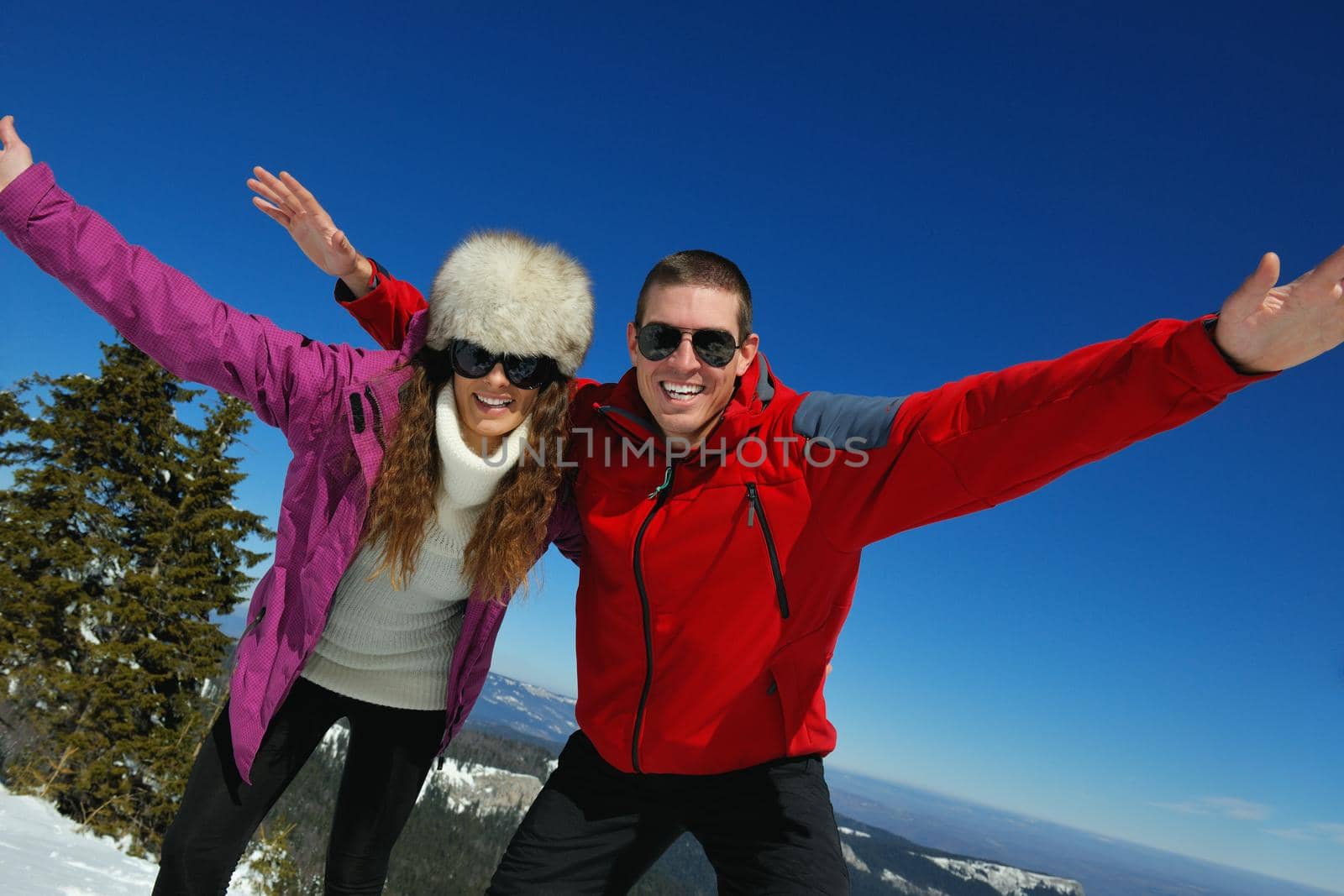 Happy young couple has fun on fresh snow at beautiful winter sunny day on vacation