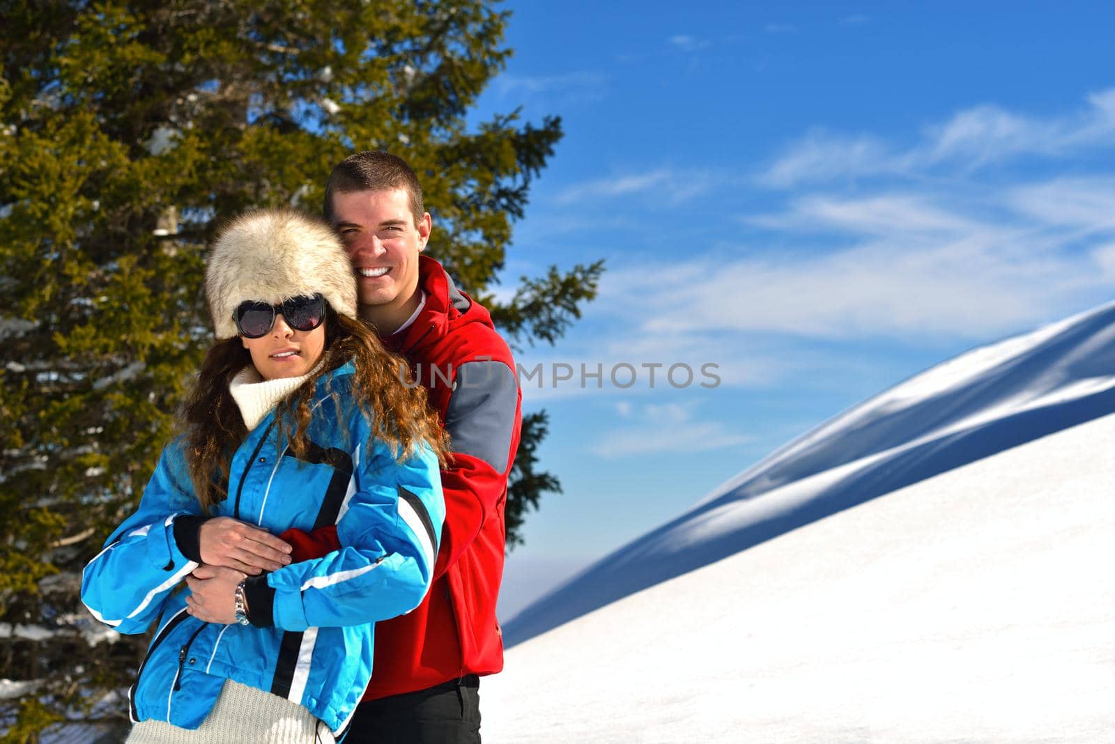 Happy young couple has fun on fresh snow at beautiful winter sunny day on relaxing vacation