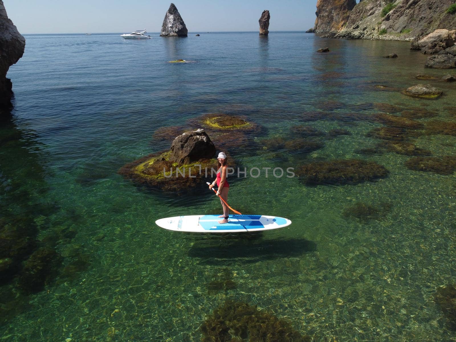 Young attractive brunette woman in red swimsuit, swimming on kayak around volcanic rocks, like in Iceland. Back view. Christmas holiday vacation and travel concept.