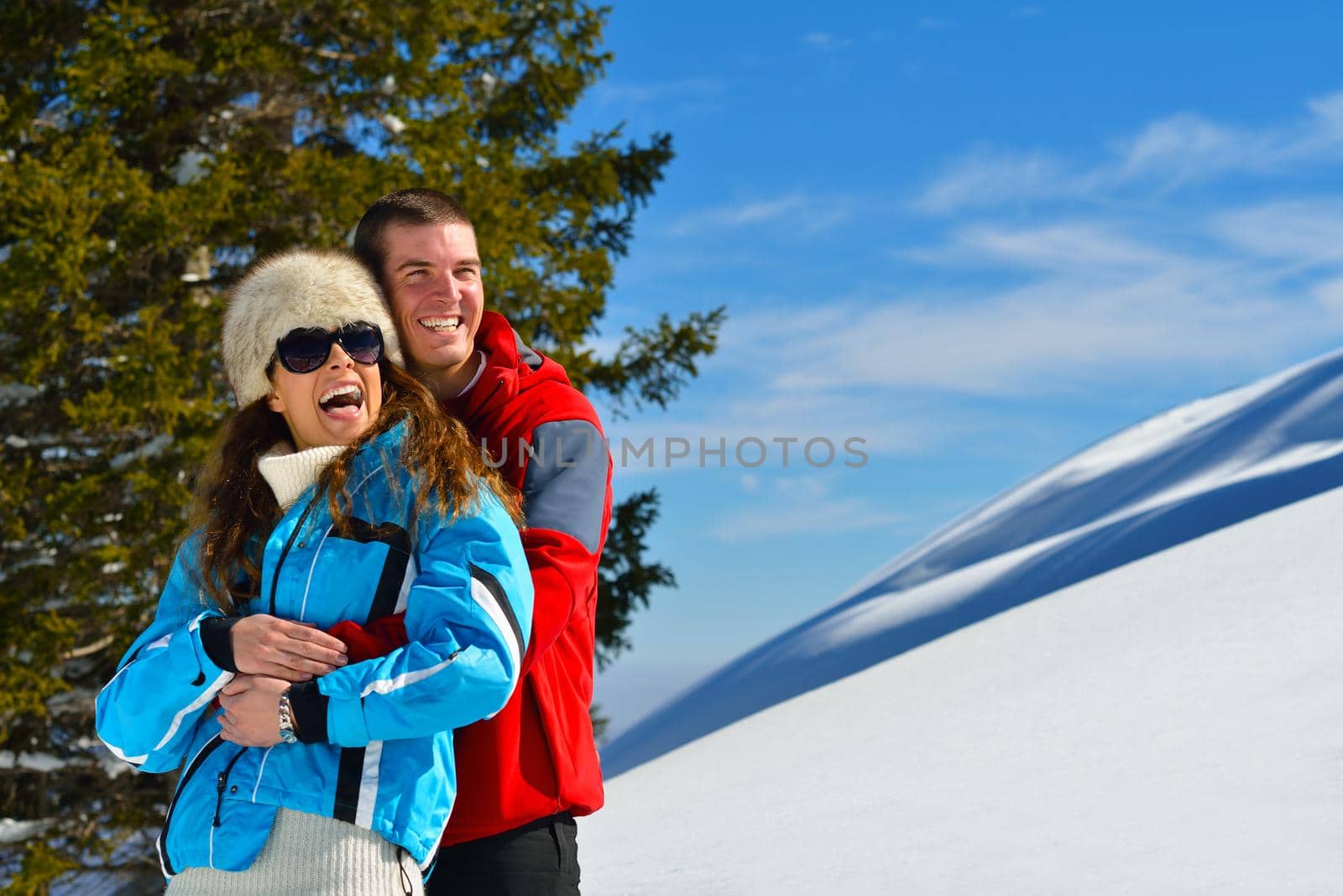 Happy young couple has fun on fresh snow at beautiful winter sunny day on relaxing vacation