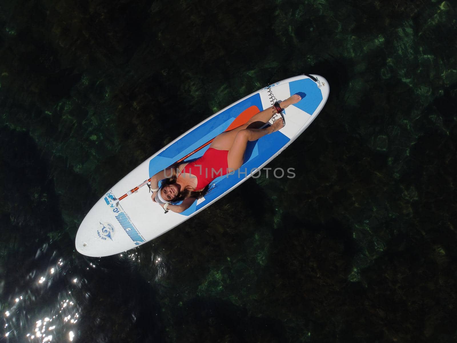 Young attractive brunette woman in red swimsuit, swimming on kayak around volcanic rocks, like in Iceland. Back view. Christmas holiday vacation and travel concept.