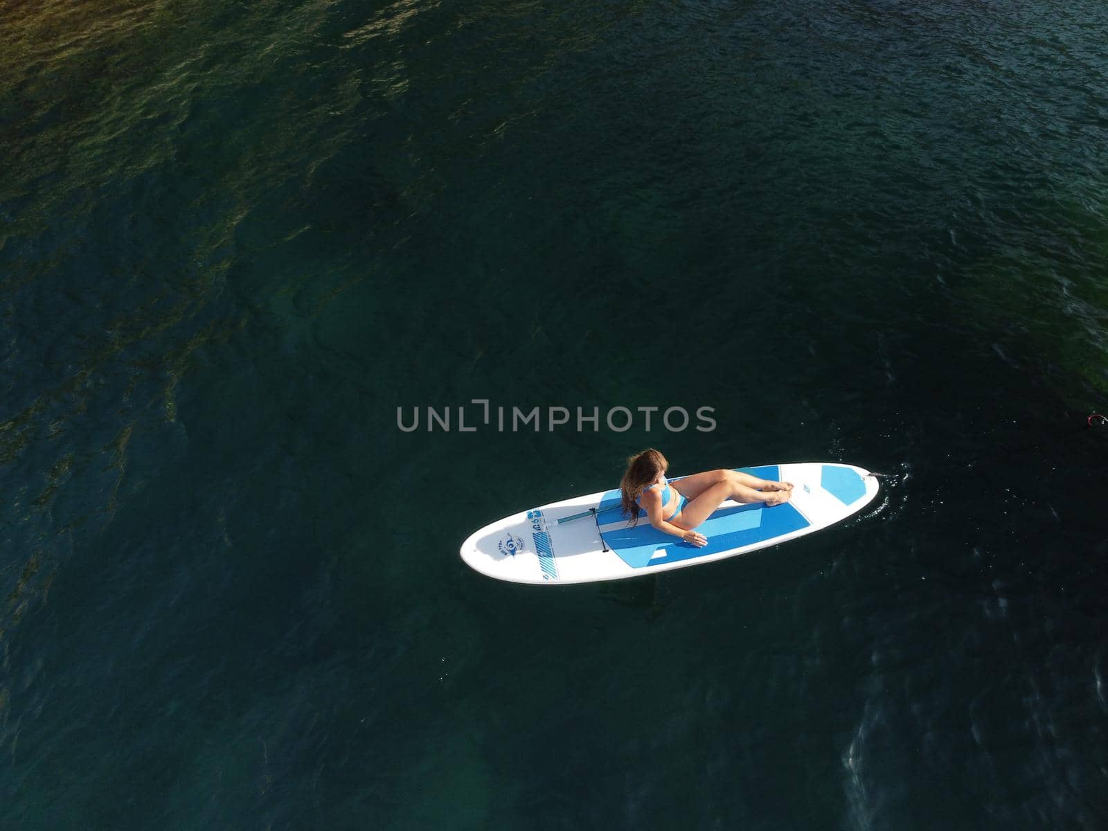 Young attractive brunette woman in red swimsuit, swimming on kayak around volcanic rocks, like in Iceland. Back view. Christmas holiday vacation and travel concept.