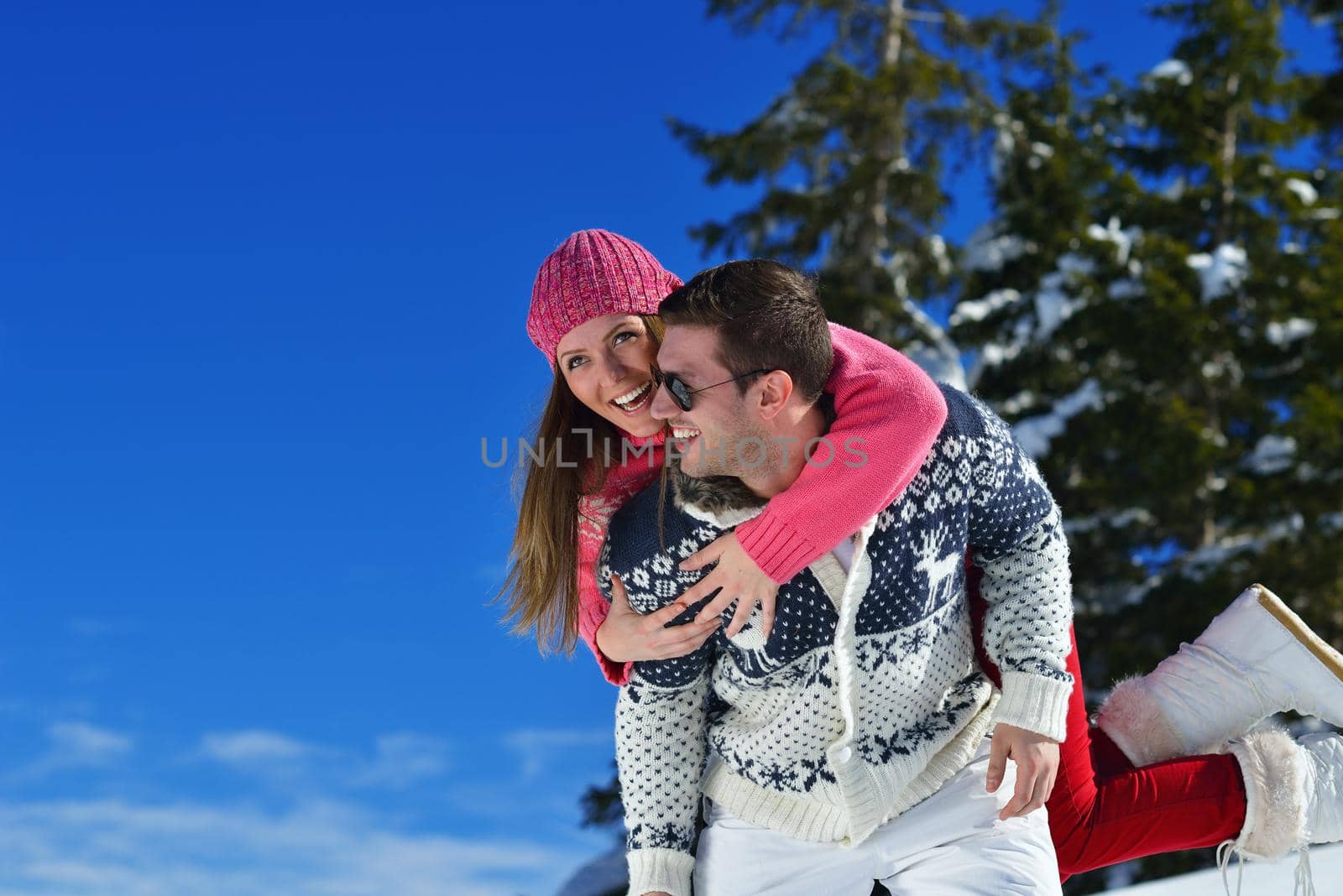 Happy young couple has fun on fresh snow at beautiful winter sunny day on vacation