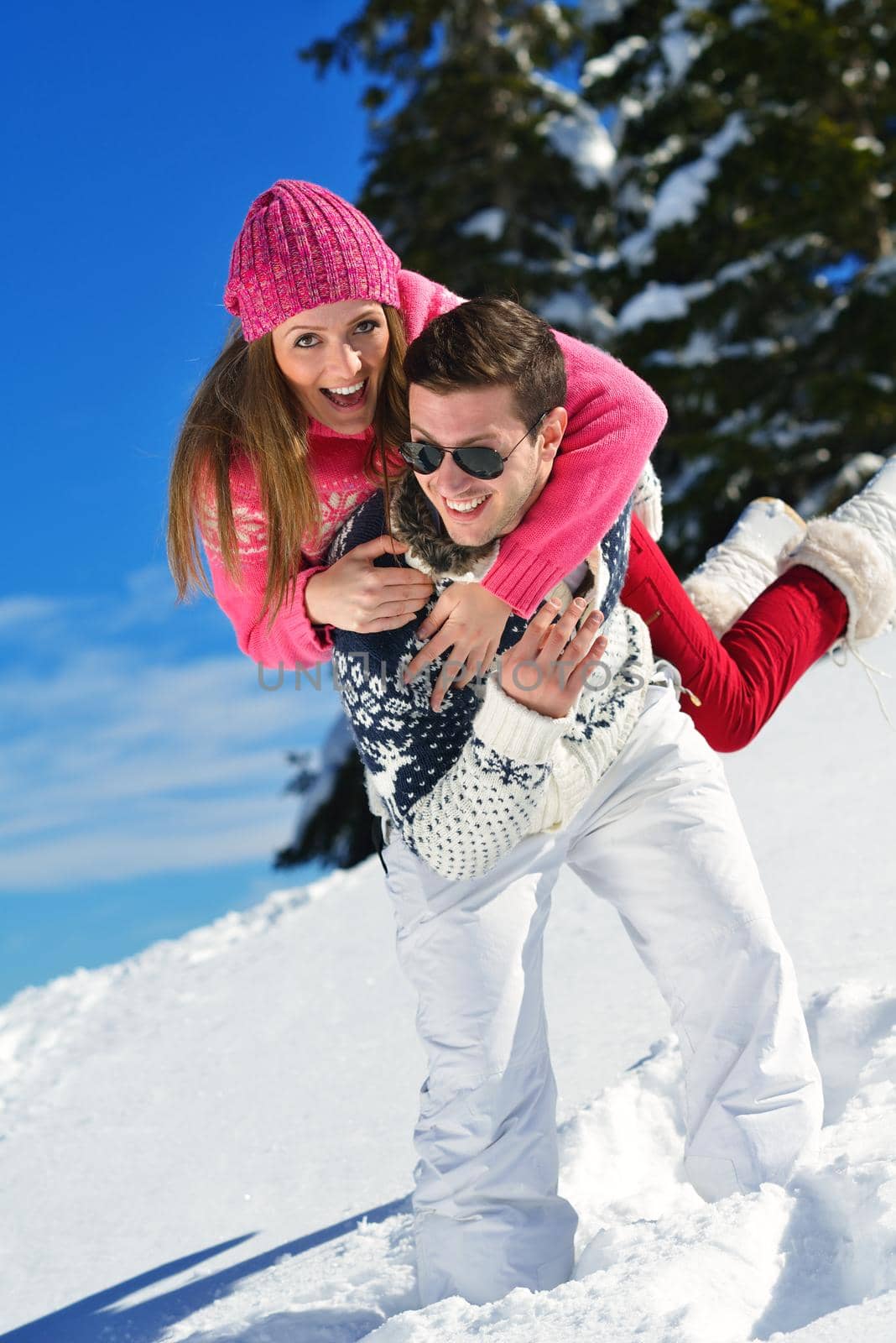 Happy young couple has fun on fresh snow at beautiful winter sunny day on vacation