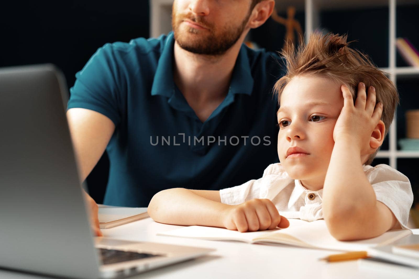 Young boy sitting with his father at the table and using laptop for study