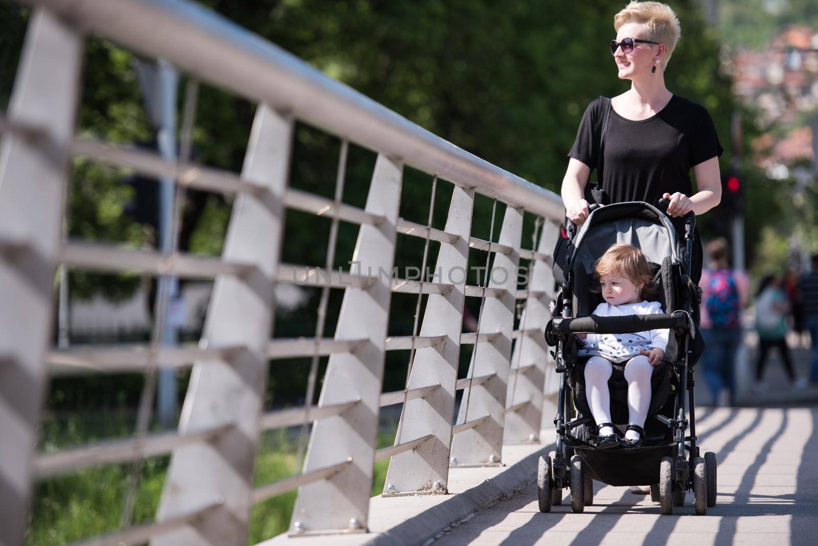 beautiful young mother with blond hair and sunglasses pushed her baby daughter in a stroller on a summer day