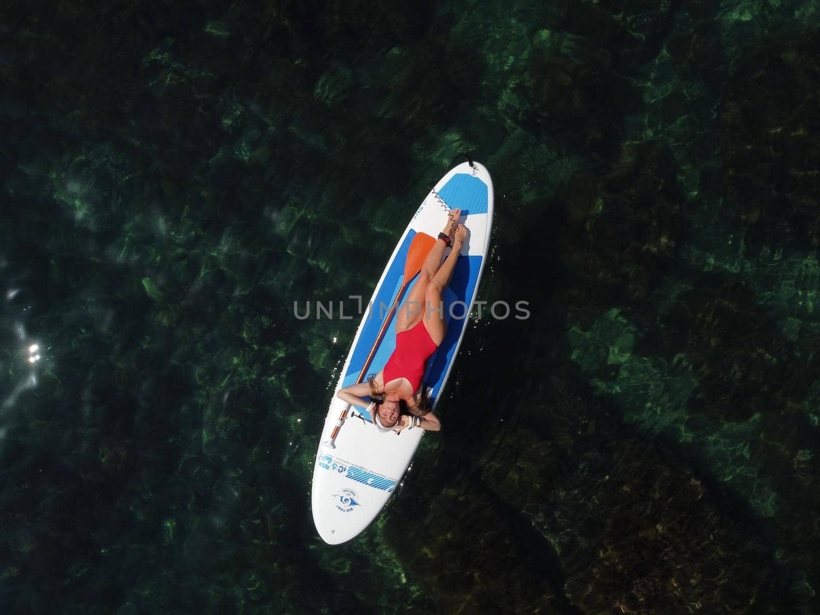 Young attractive brunette woman in red swimsuit, swimming on kayak around volcanic rocks, like in Iceland. Back view. Christmas holiday vacation and travel concept.