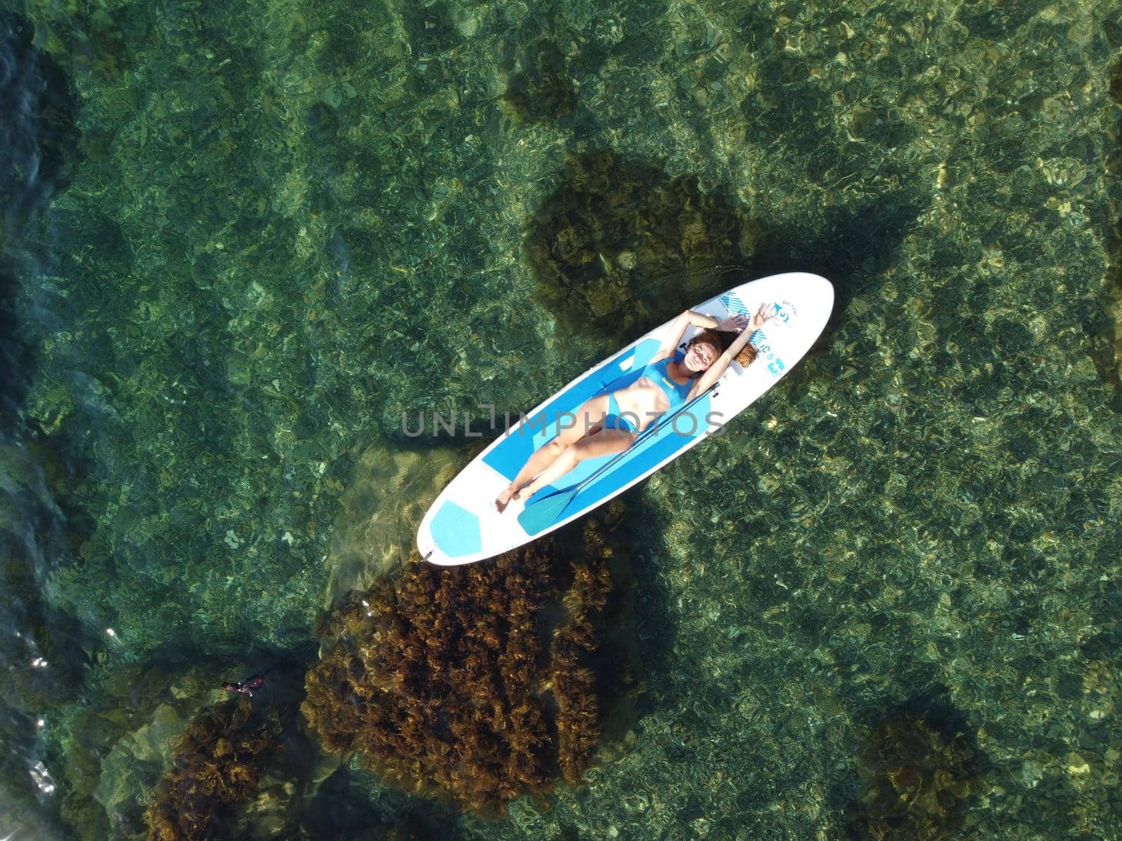 Young attractive brunette woman in red swimsuit, swimming on kayak around volcanic rocks, like in Iceland. Back view. Christmas holiday vacation and travel concept.