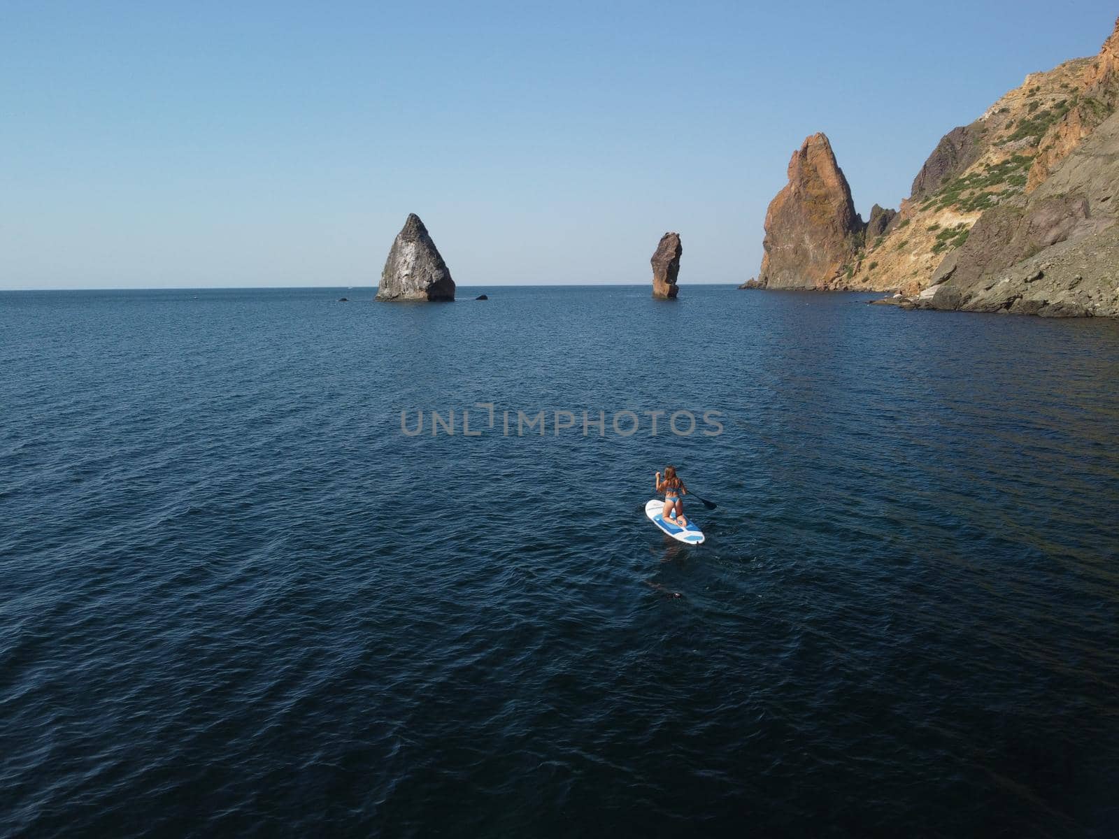 Young attractive brunette woman in red swimsuit, swimming on kayak around volcanic rocks, like in Iceland. Back view. Christmas holiday vacation and travel concept.
