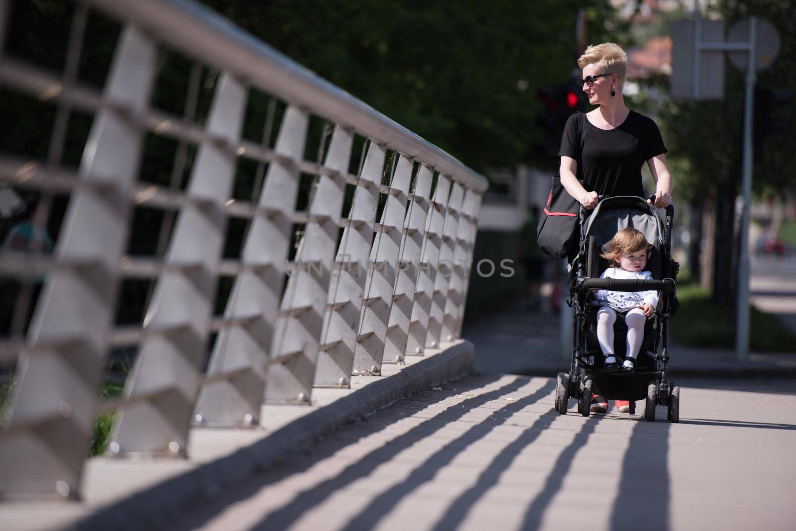 beautiful young mother with blond hair and sunglasses pushed her baby daughter in a stroller on a summer day